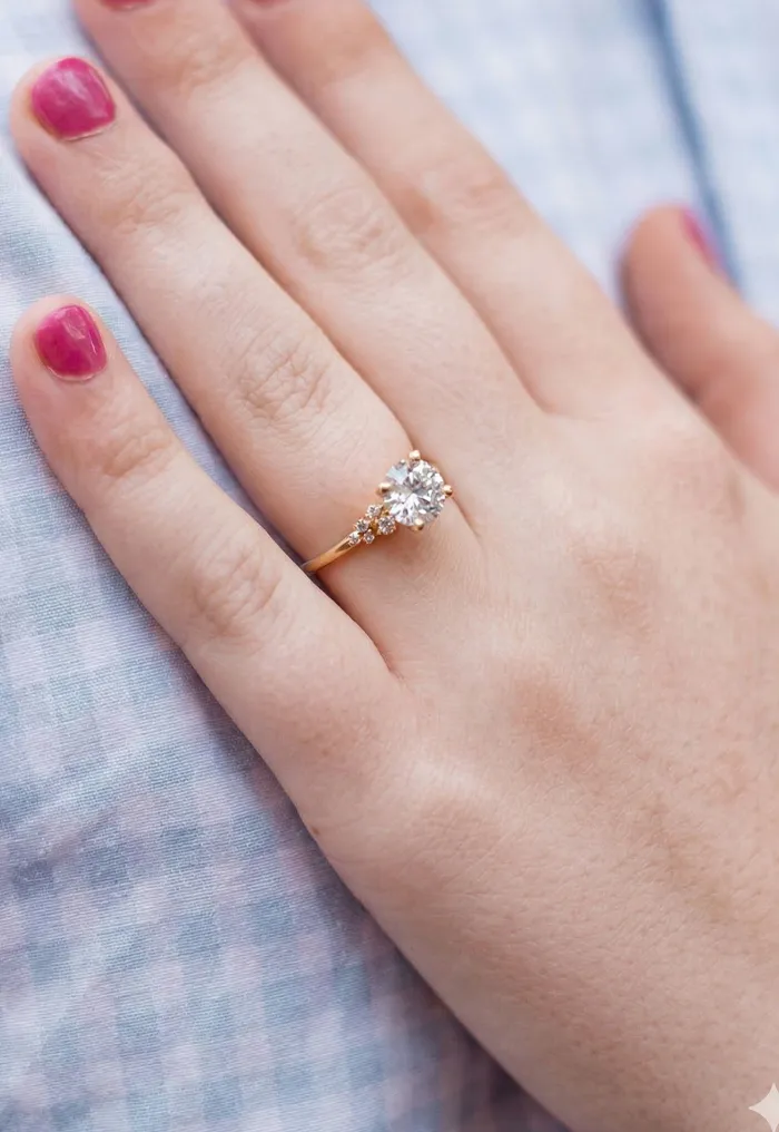 A hand with a diamond ring rests on a blue checkered fabric.