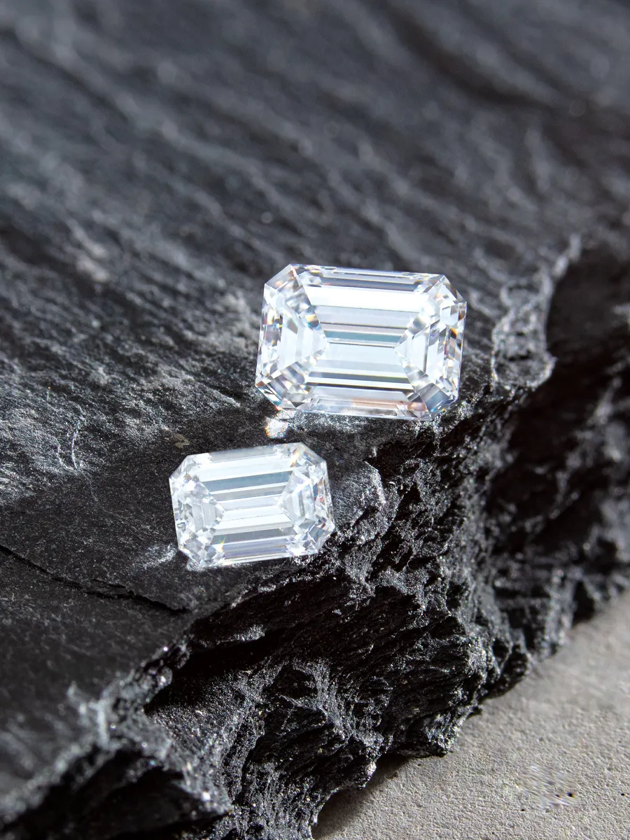 Two emerald-cut diamonds on textured black stone surface.