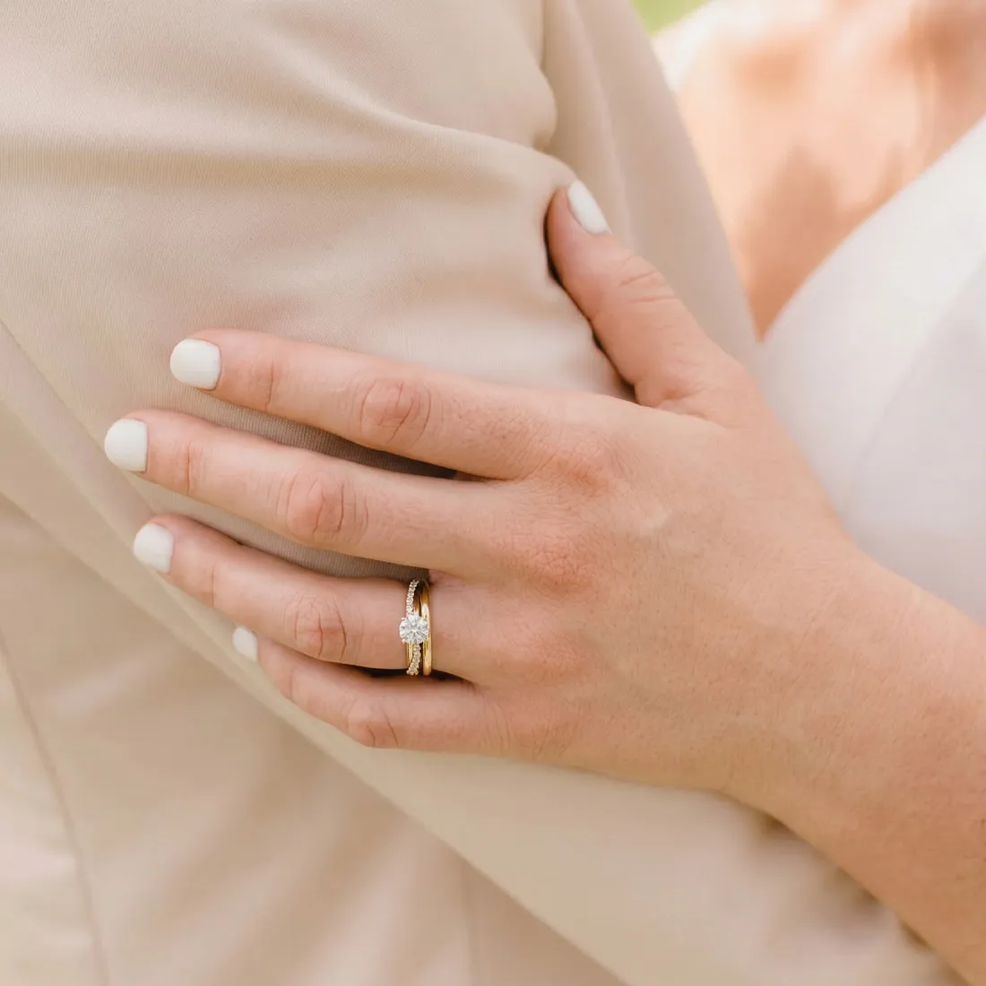 Close-up of a hand with white nails and a diamond ring resting on a beige fabric.