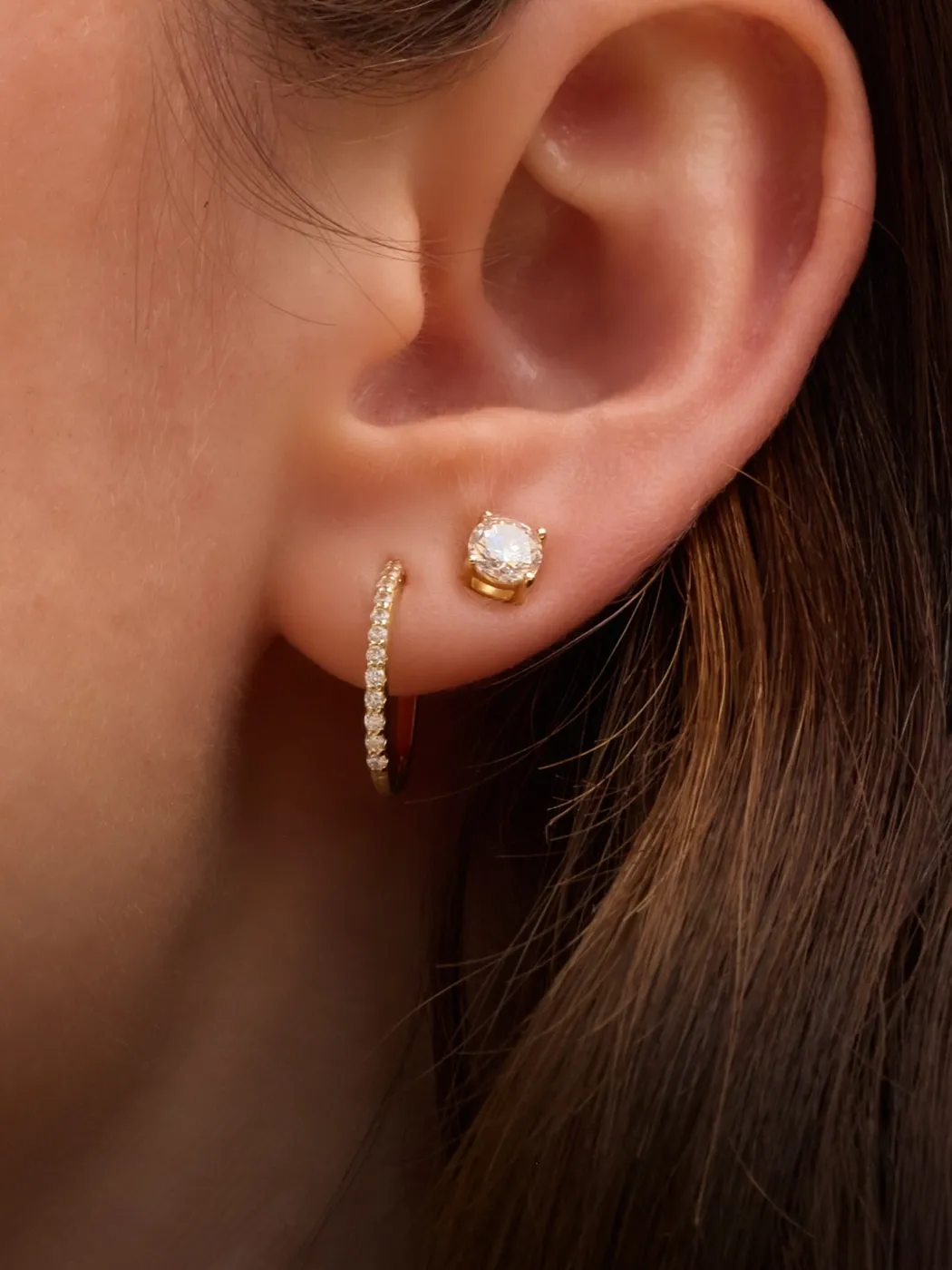 Close-up of an ear with a diamond stud and a gold hoop earring.