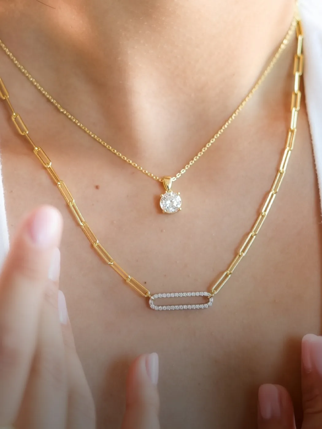 Two gold necklaces on a neck, one with a diamond pendant and the other with a diamond-studded link.
