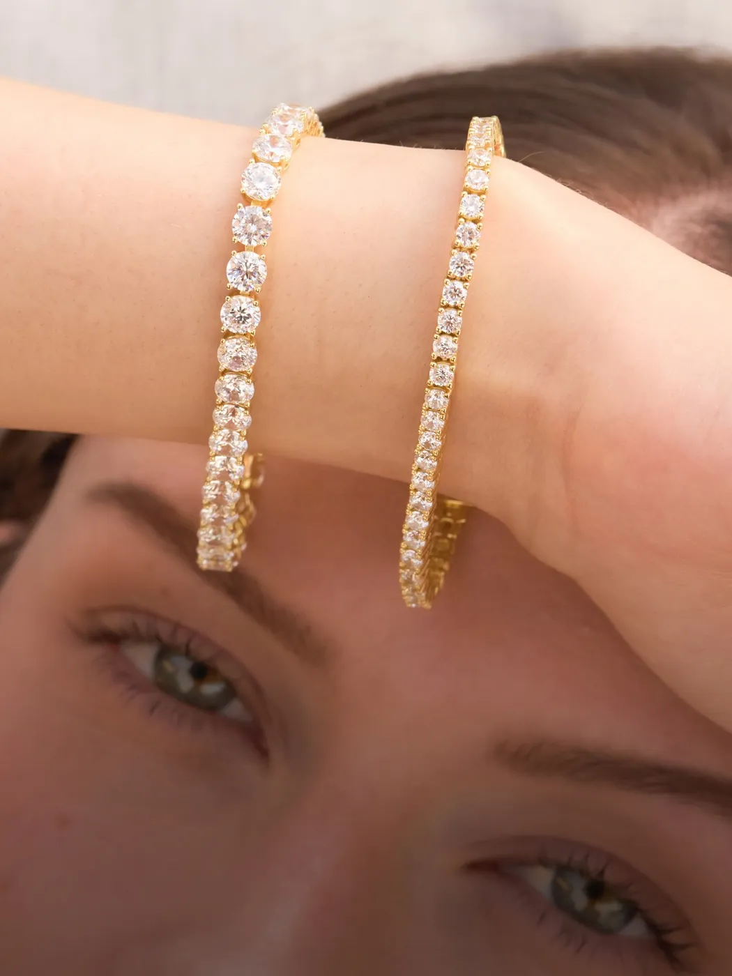 Two gold diamond bracelets on a person's arm, with their face partially visible.