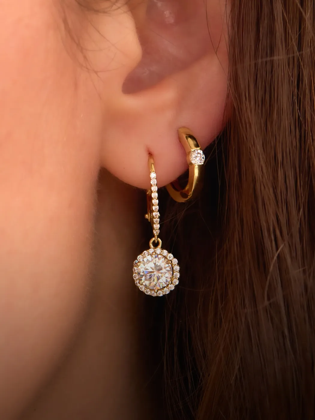 Close-up of ear with two gold hoop earrings, one with a large diamond.