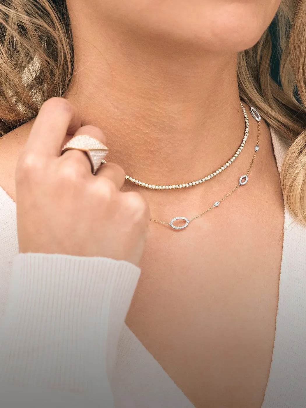 Close-up of a person wearing layered diamond necklaces and a ring.