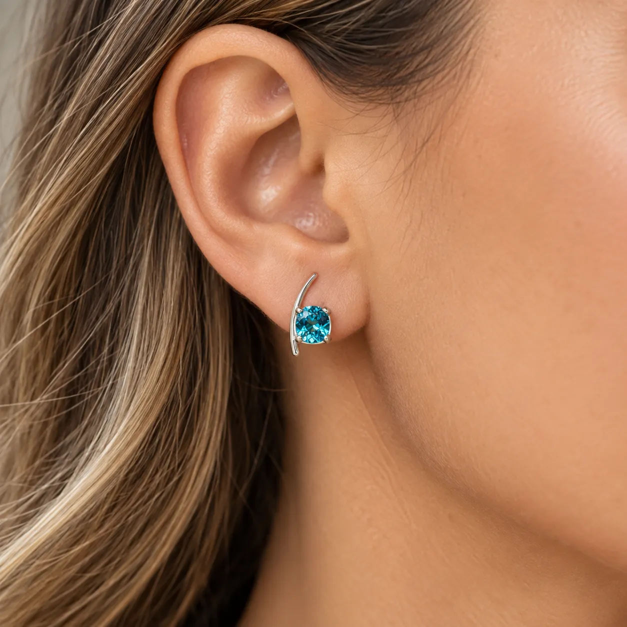 Close-up of an ear wearing a custom white gold earring with a blue topaz on a curved bar