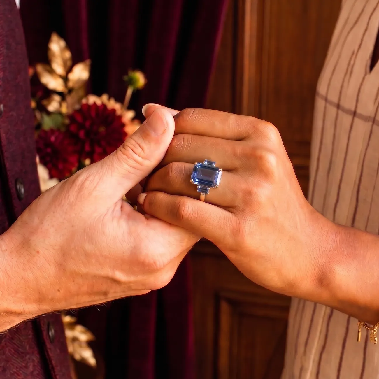 Two hands holding, one wearing a ring with a large blue gemstone.