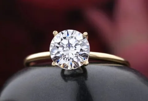 Gold solitaire diamond engagement ring on black surface.