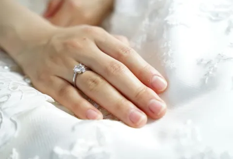 Engagement ring on hand with wedding dress.
