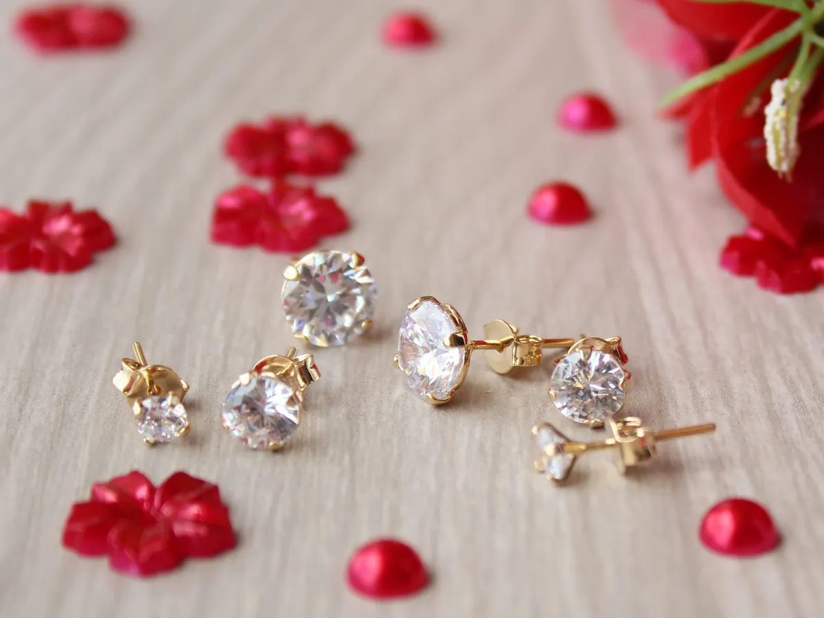 Three sets of gold diamond earrings displayed with flowers