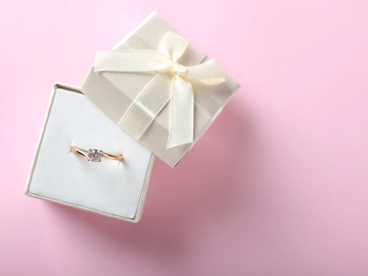 Gold diamond ring in jewelry box on pink background
