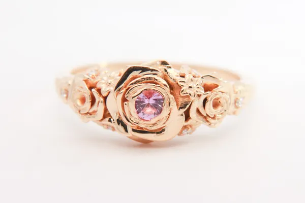Custom rose gold ring with sculpted roses around a pink center stone, front view
