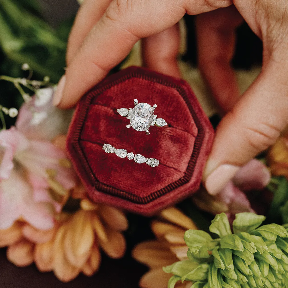 A hand with two gold rings, one with a large oval stone, over a floral background.