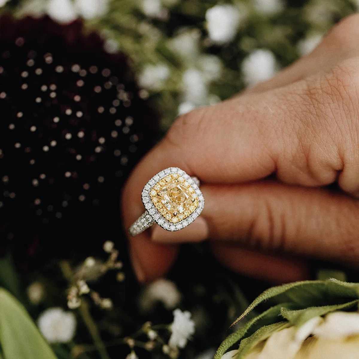 Diamond ring in a green velvet box with blurred floral background.