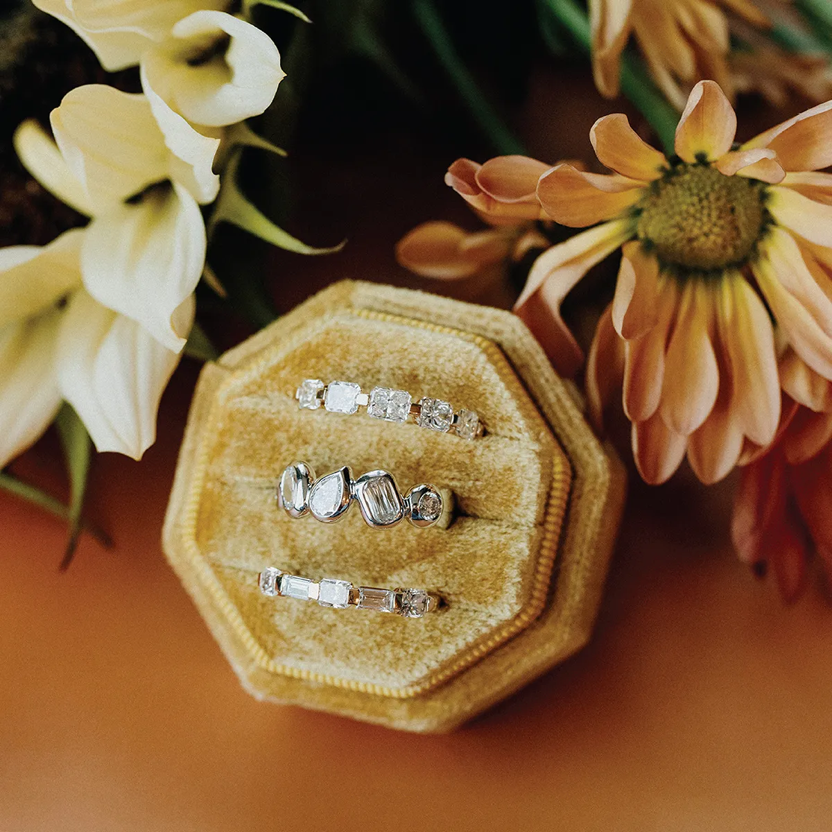 Three diamond rings displayed in a beige jewelry box with a floral background.