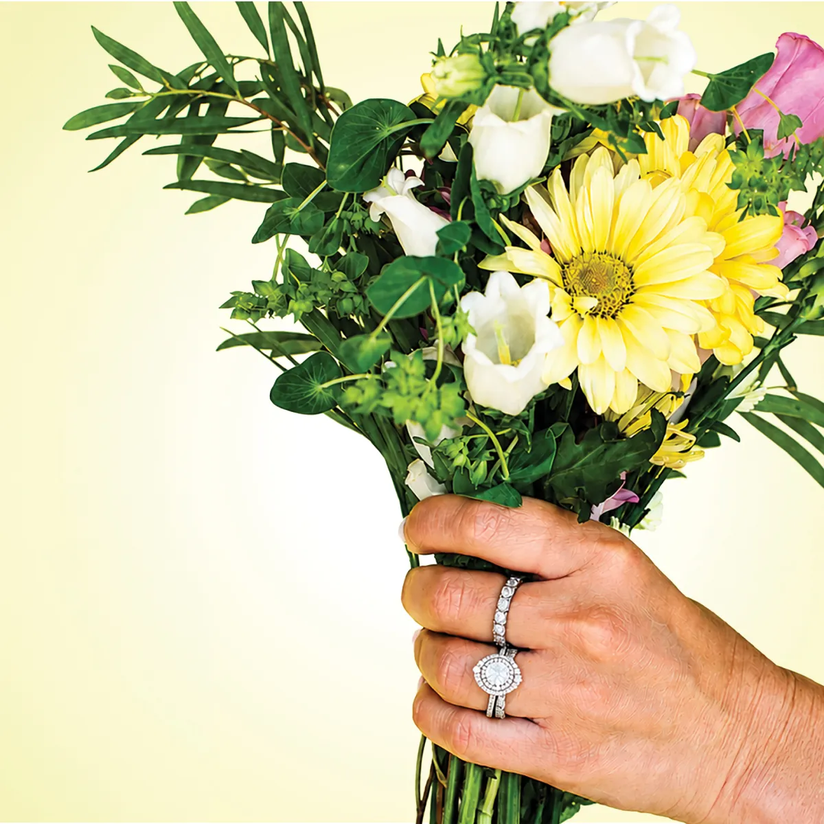 Hand holding a bouquet of flowers, showcasing a diamond ring.