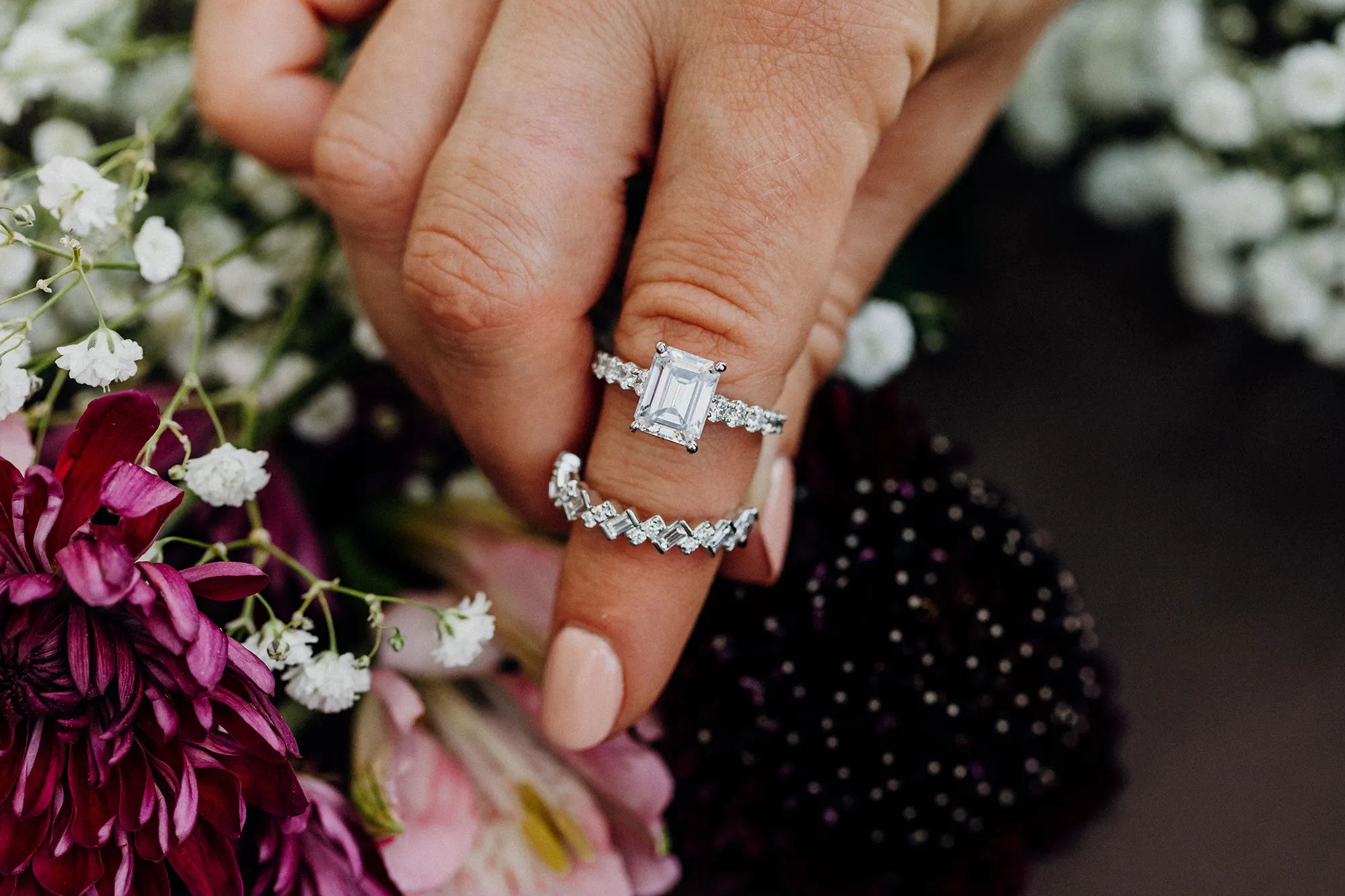 Elegant diamond engagement ring set on a hand, surrounded by greenery.