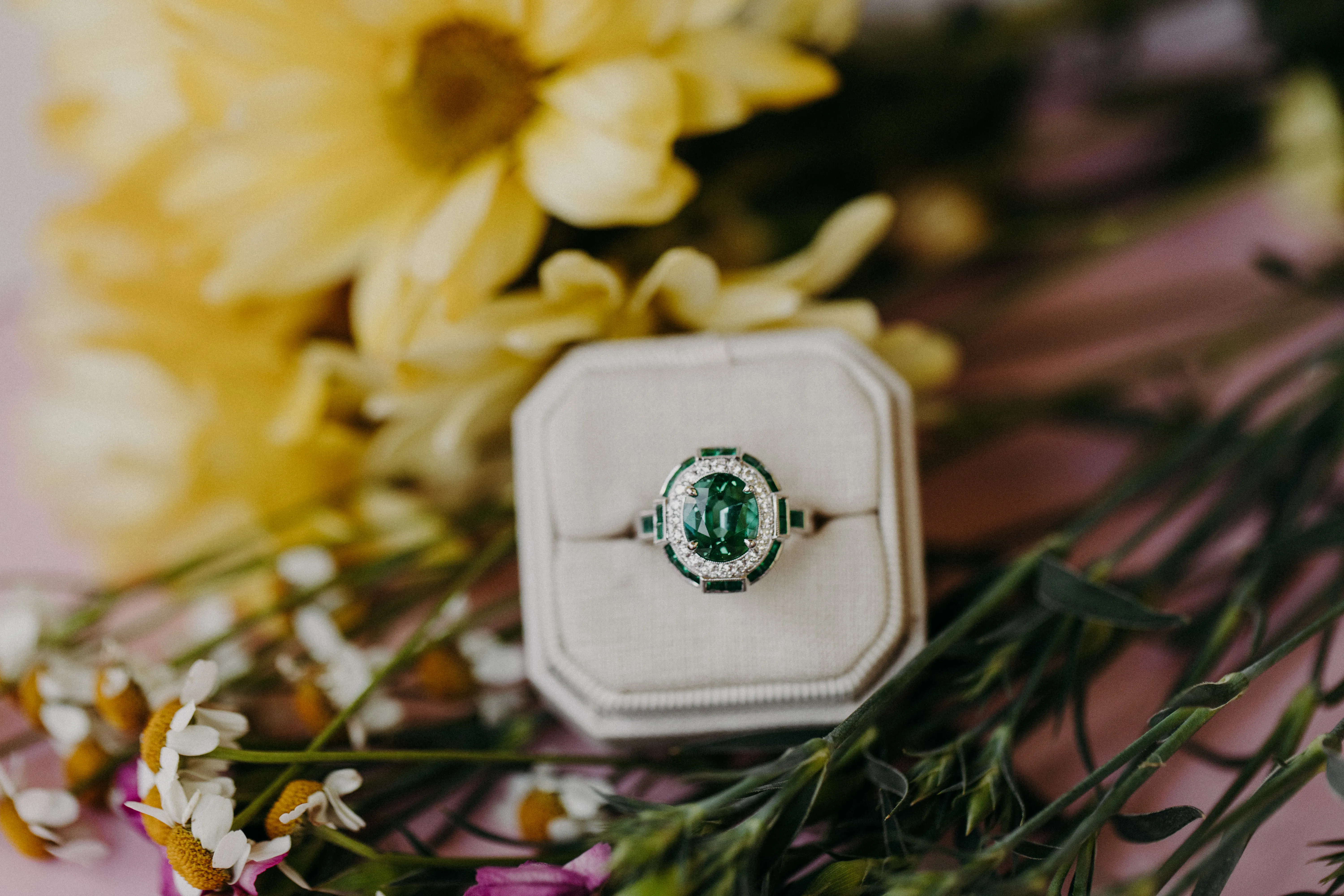 Emerald ring in a box with flowers. Click to explore fashion rings.