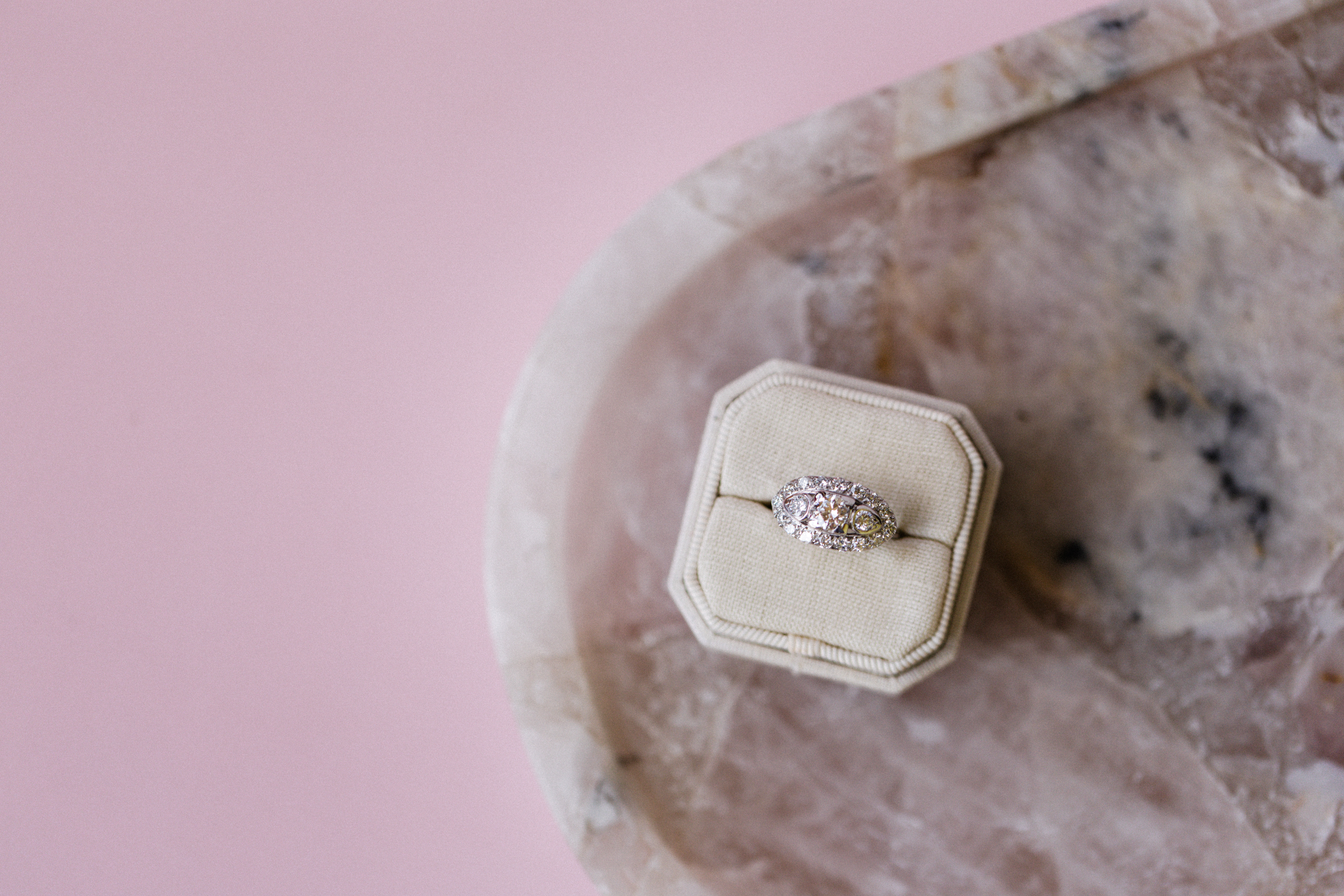 Diamond ring in a cream box on a marble surface with a pink background.