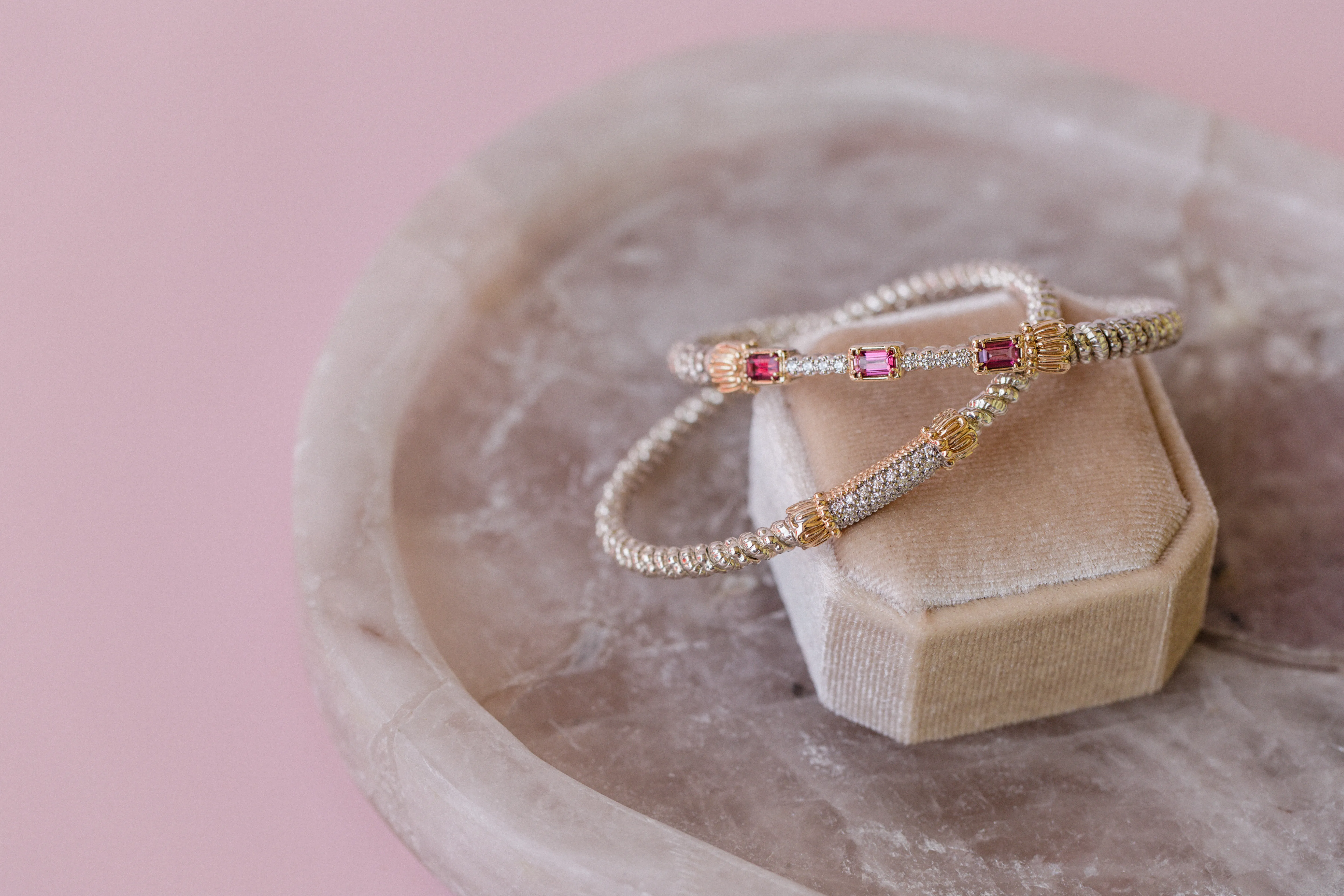 Two elegant Vahan Silver and 14K gold bracelets with pink and gold accents displayed on a velvet box against a pink background.
