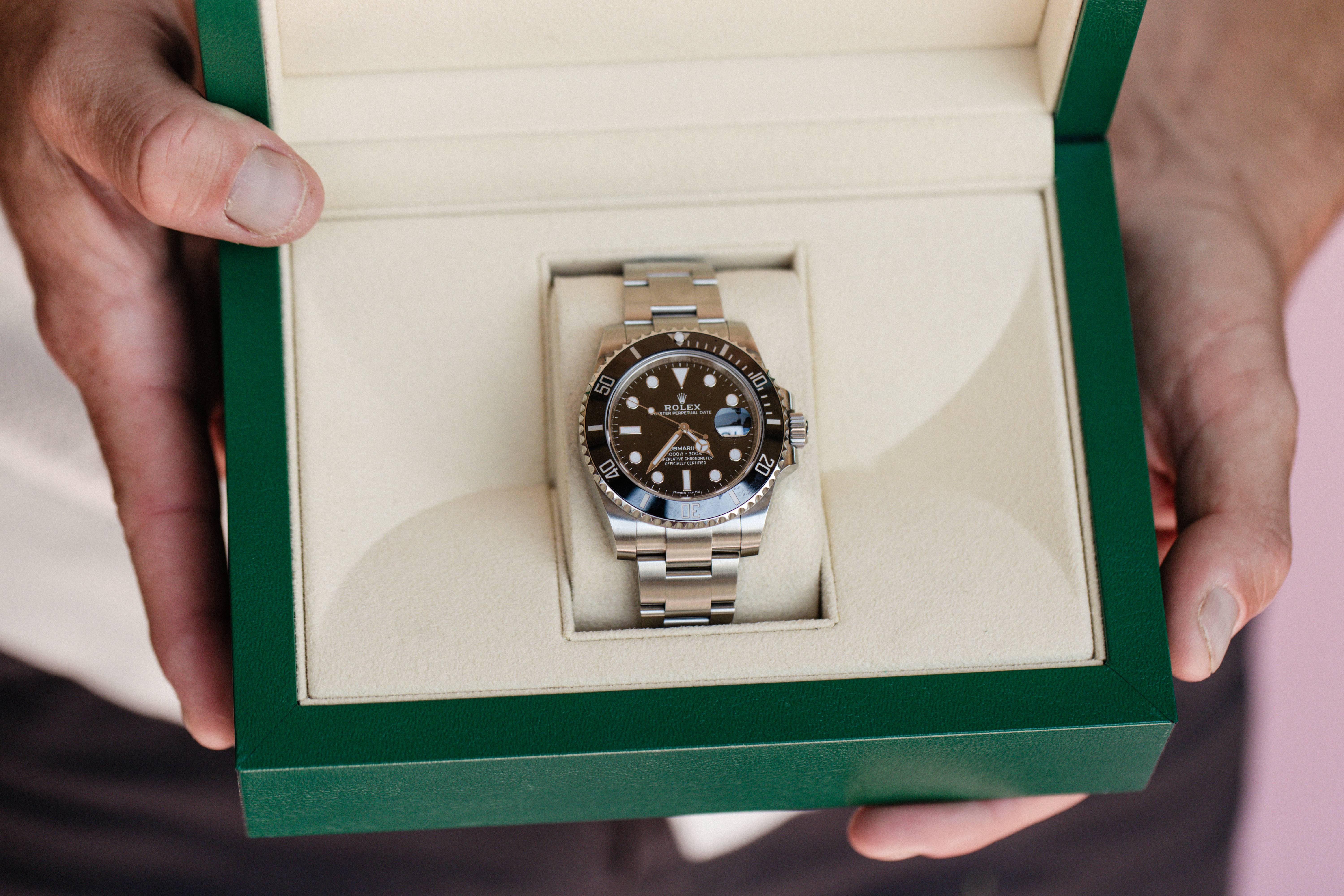 A luxury watch in a green box is held open. Click to view pre-owned watches.