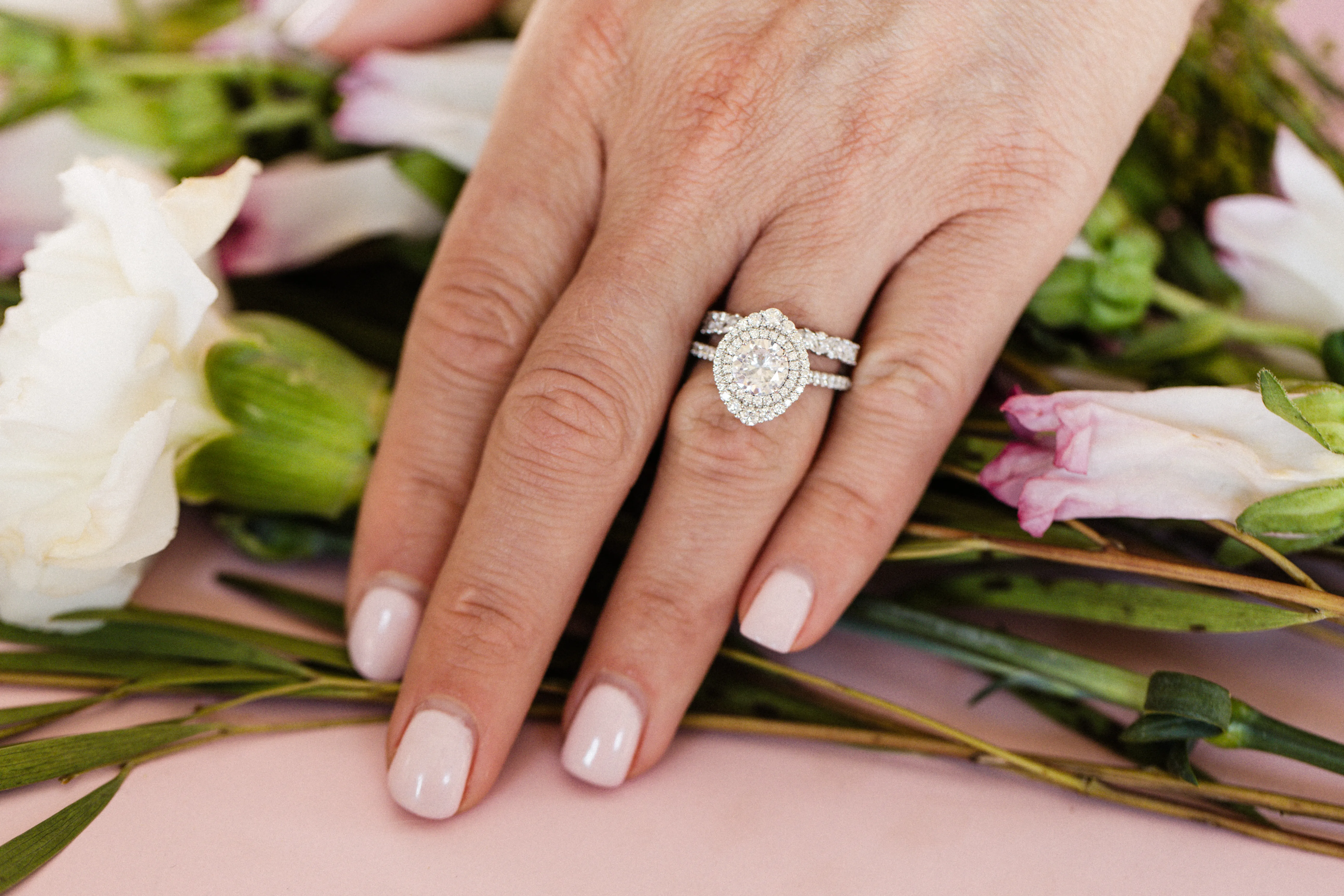 Elegant diamond engagement ring set on a hand, surrounded by greenery.