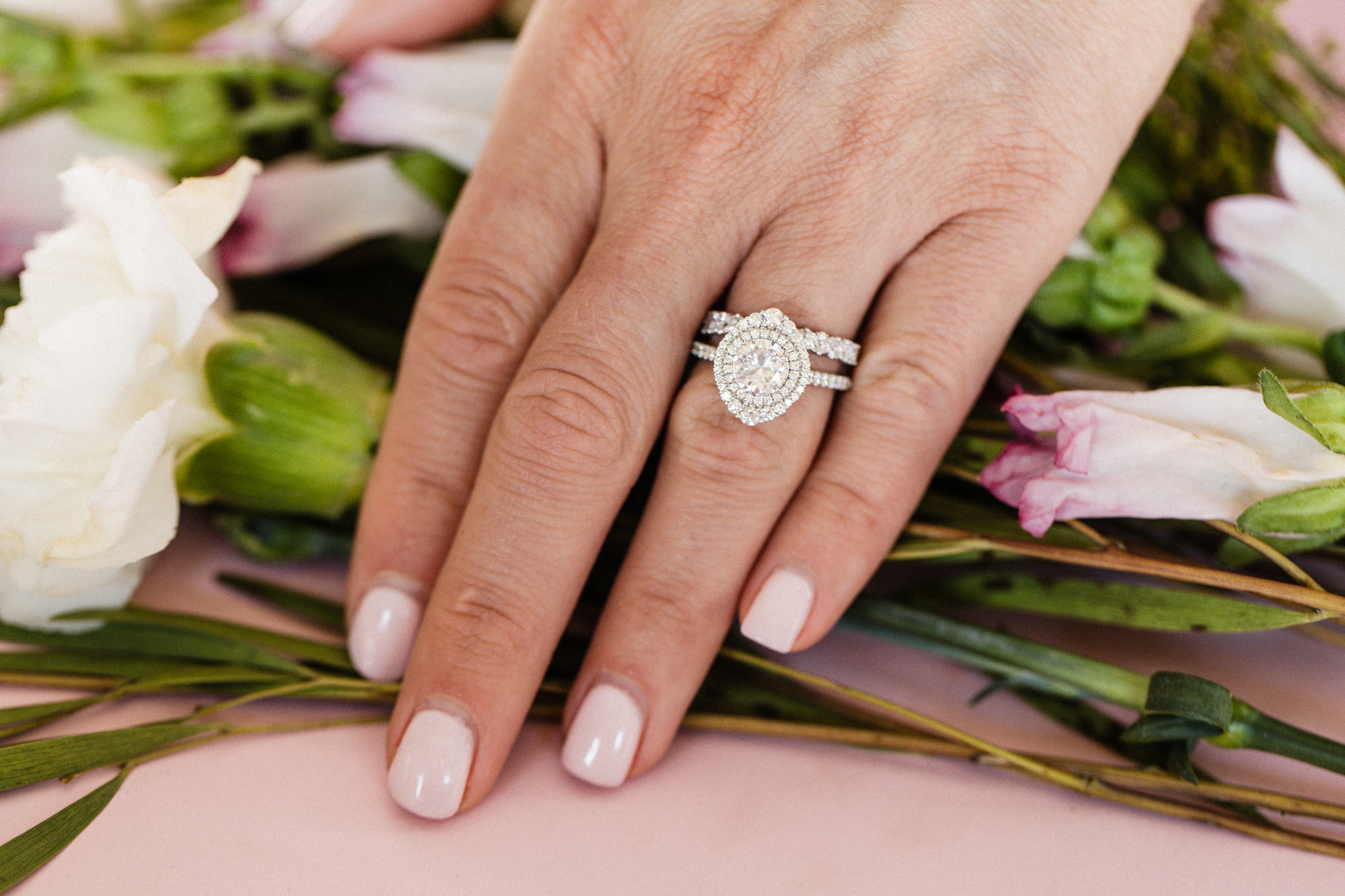 Elegant diamond engagement ring set on a hand, surrounded by greenery.