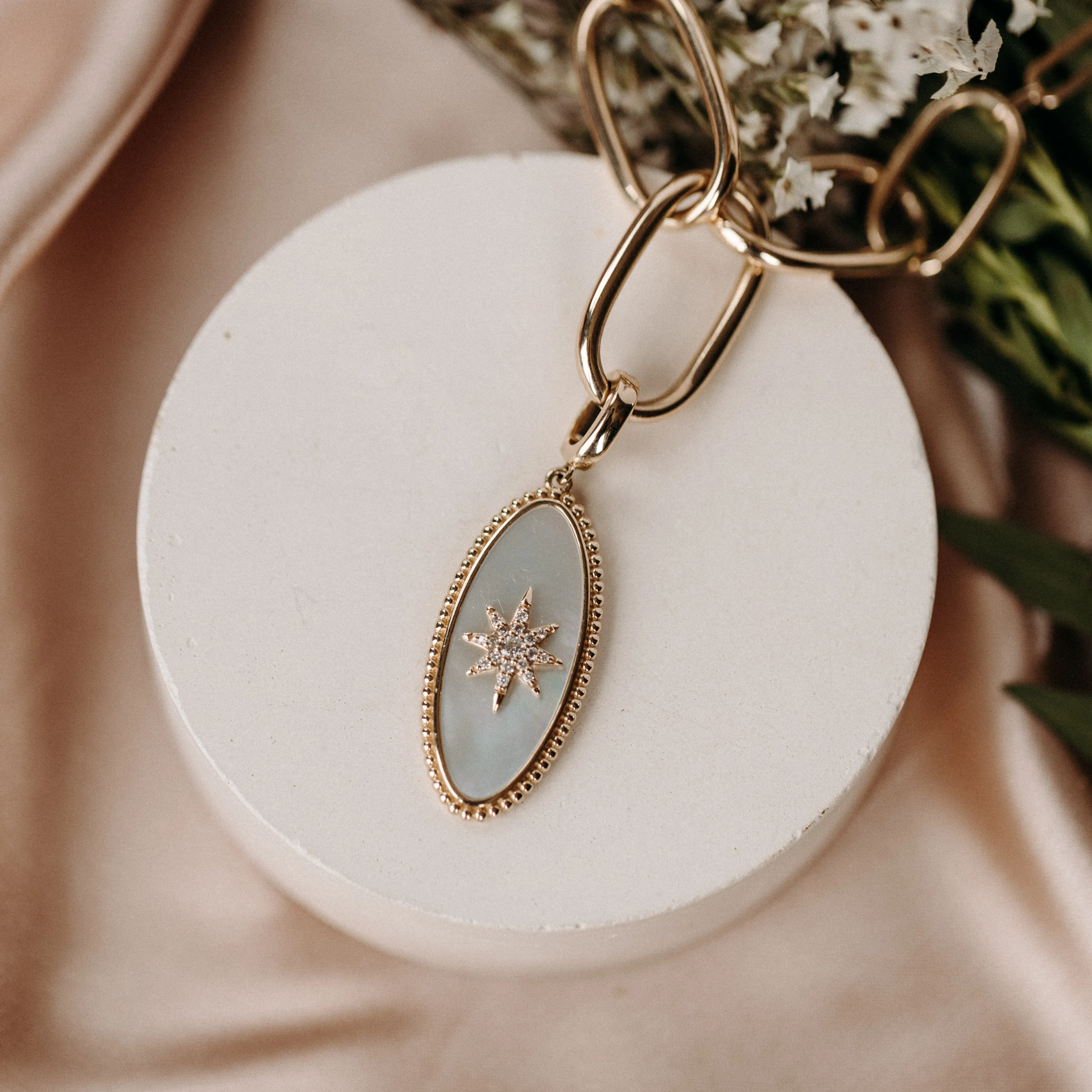 Gold necklace with an oval pendant featuring a star design on a soft background.