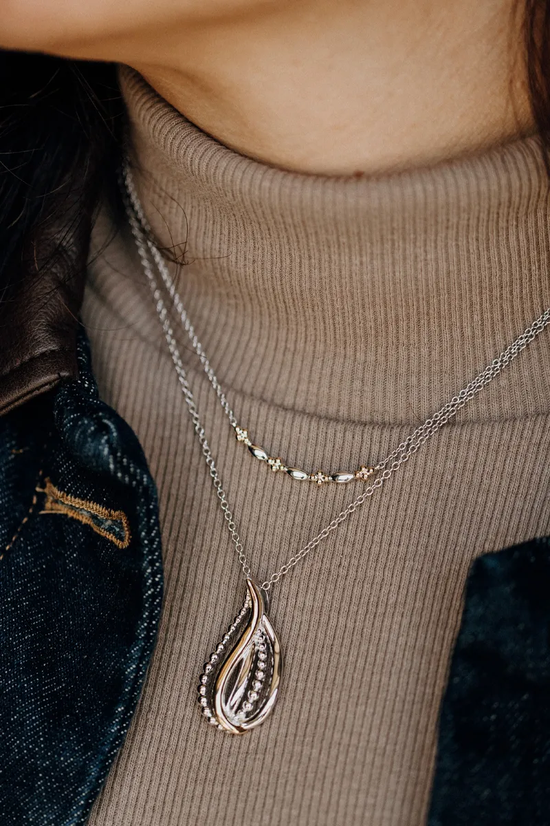 Close-up of layered necklaces featuring a teardrop pendant and delicate chain, worn over a turtleneck sweater.