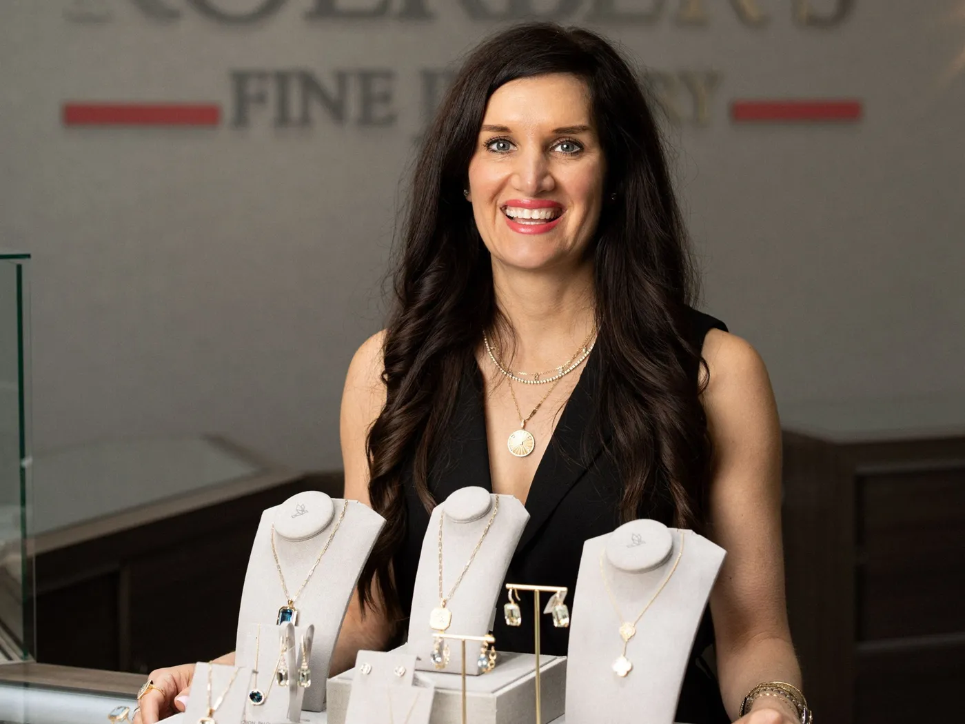 Smiling woman in a black dress showcasing fine jewelry at Koerber's Fine Jewelry in New Albany.