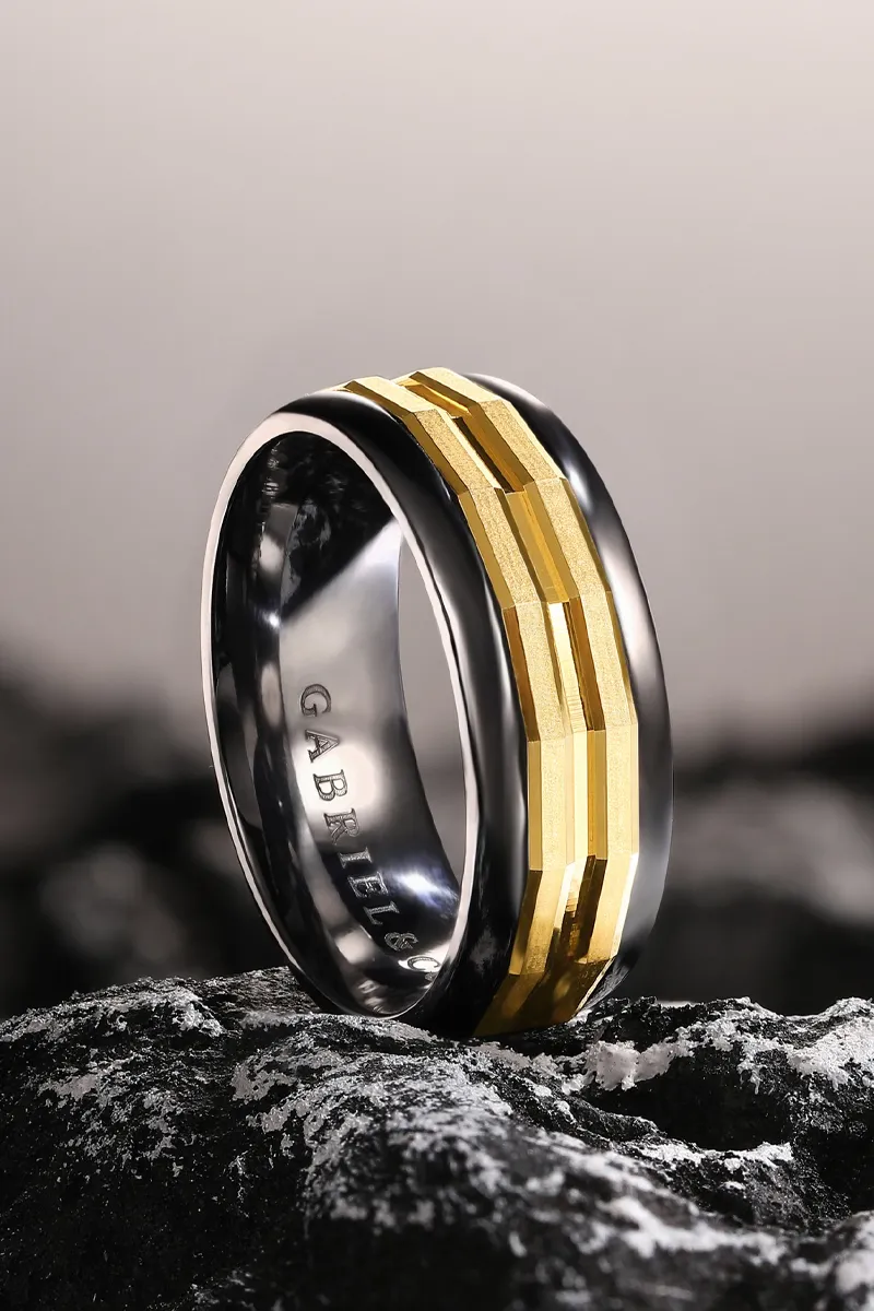 Black and gold men's wedding band displayed on a rocky surface, showcasing a modern design.