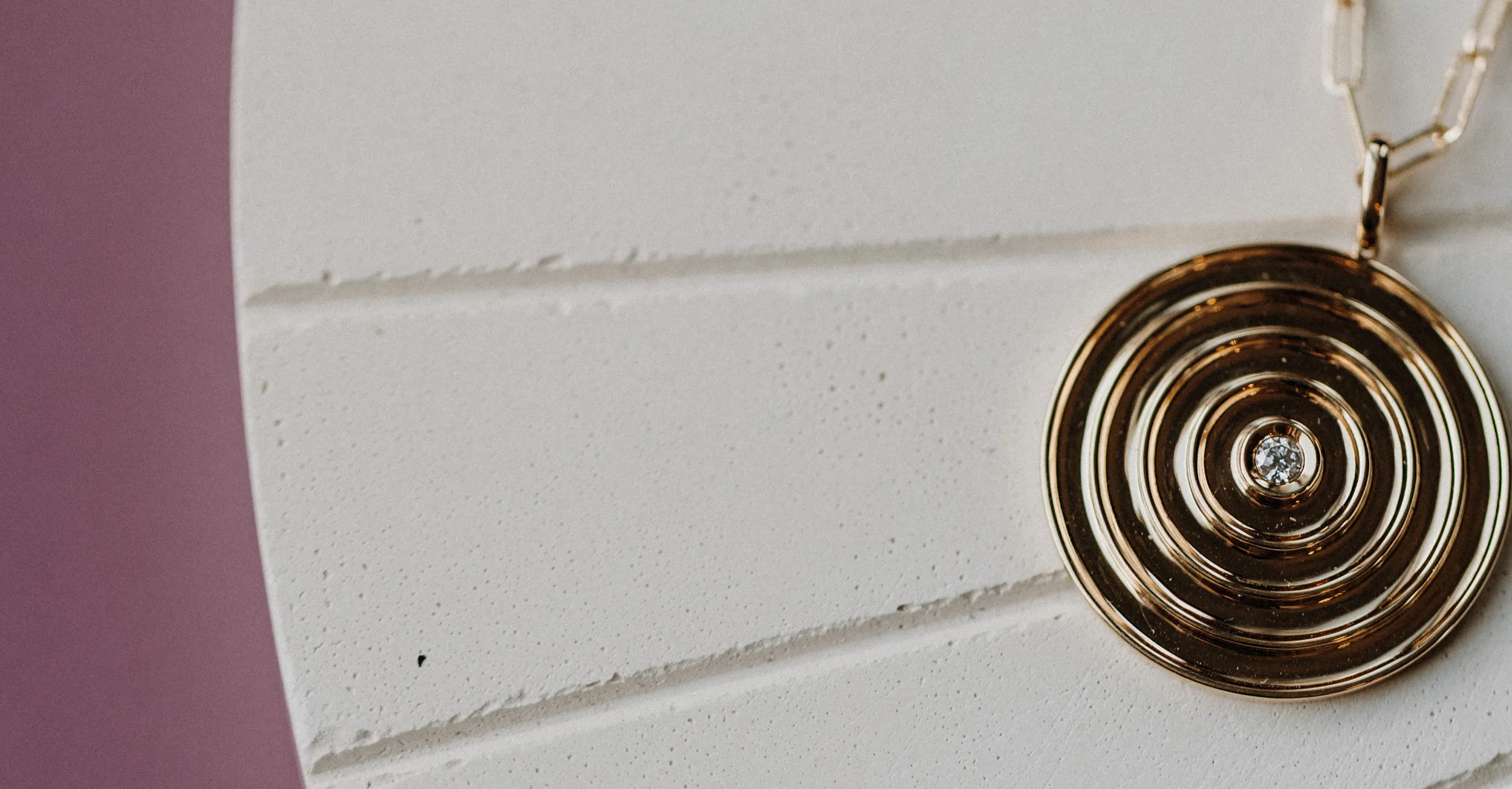 Gold spiral pendant with a diamond centerpiece on a white surface, inviting users to start a jewelry design project.