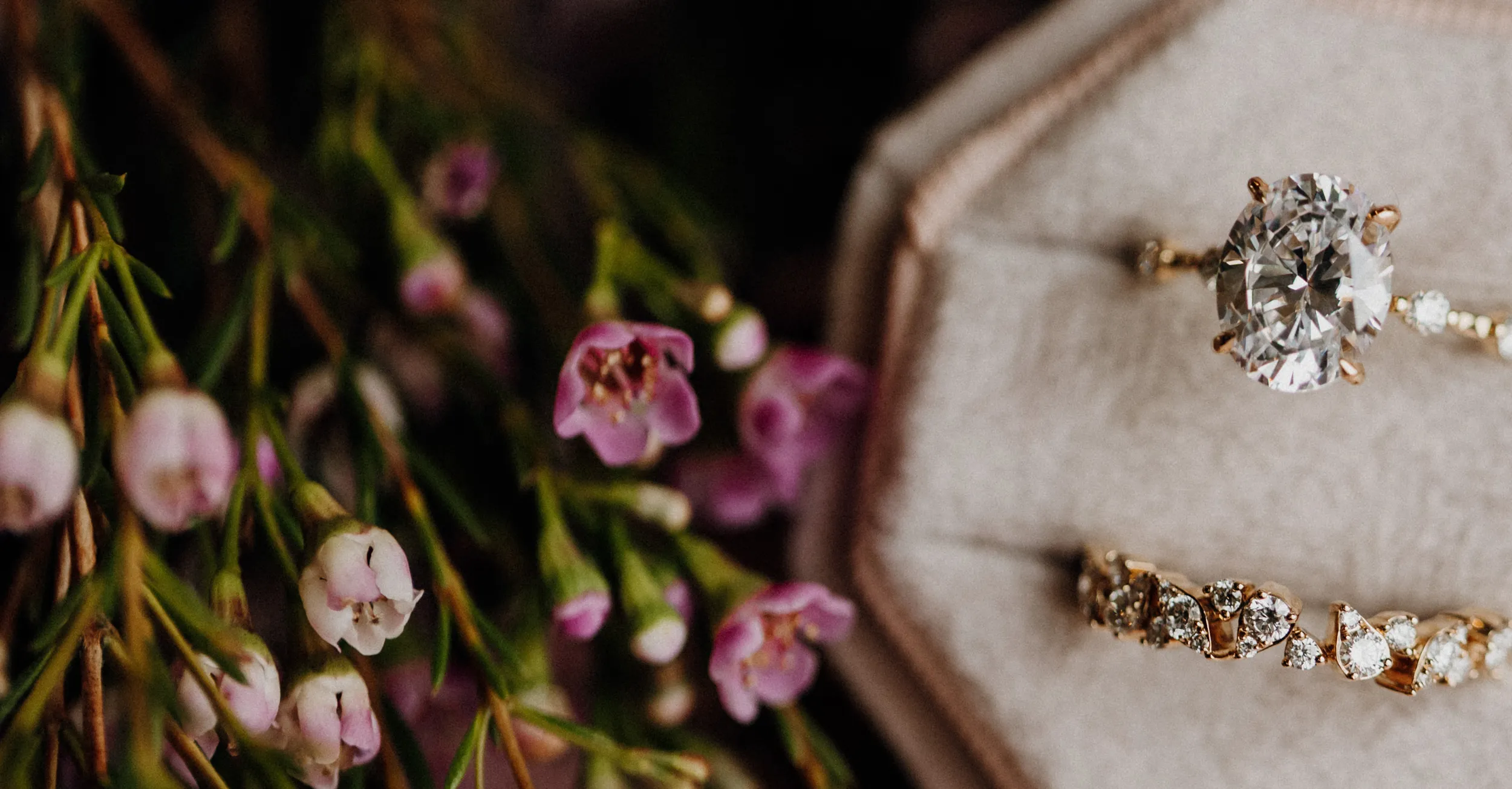 Elegant diamond rings displayed on a soft surface with delicate pink flowers in the background.