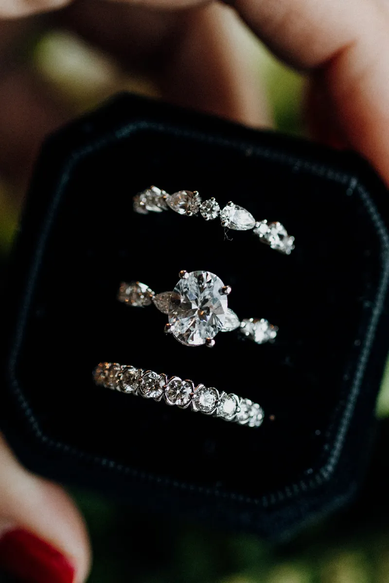Three elegant diamond rings displayed in a black velvet box, showcasing a stunning engagement ring and matching bands.