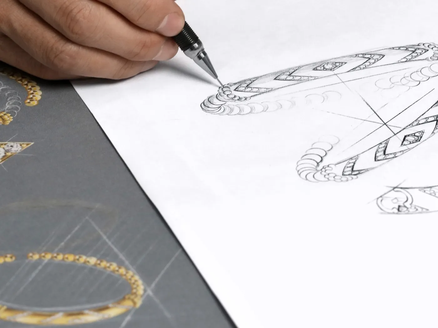 A hand sketches intricate jewelry designs on paper, showcasing creativity and craftsmanship at Koerbers Fine Jewelry in New Alba