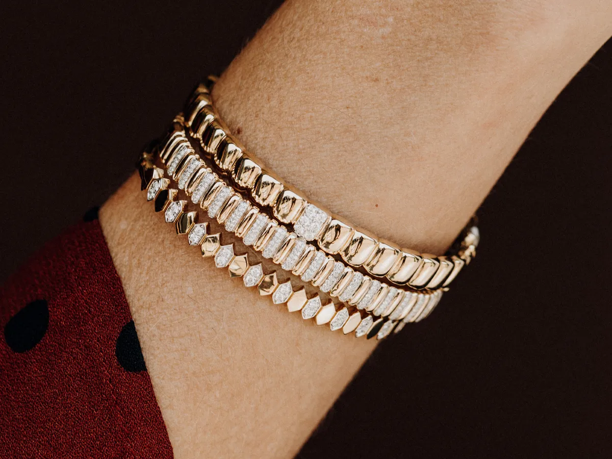 Three elegant gold bracelets with various designs worn on a wrist.