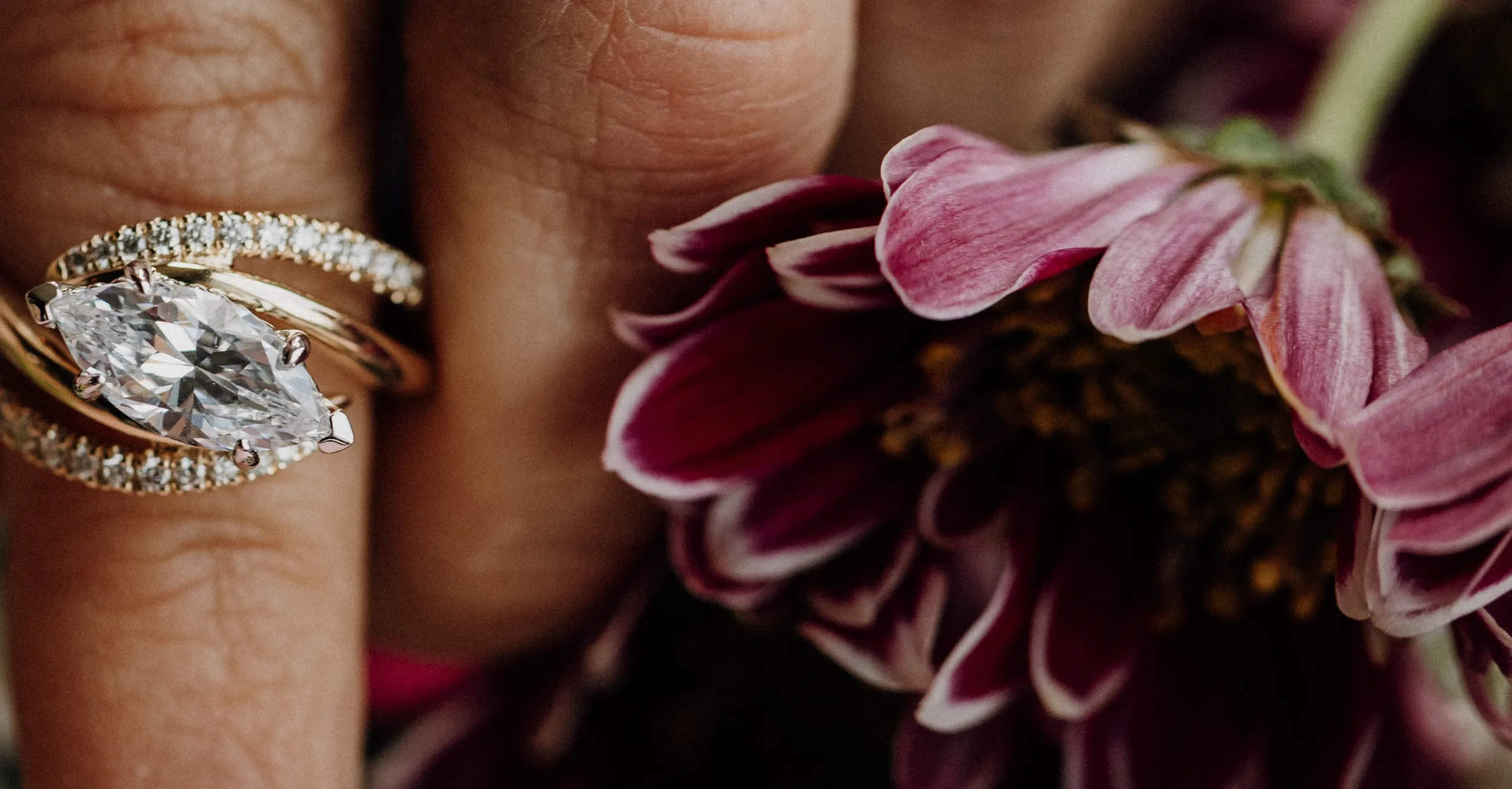 Elegant engagement ring with a marquise diamond, resting on a hand near a pink flower.