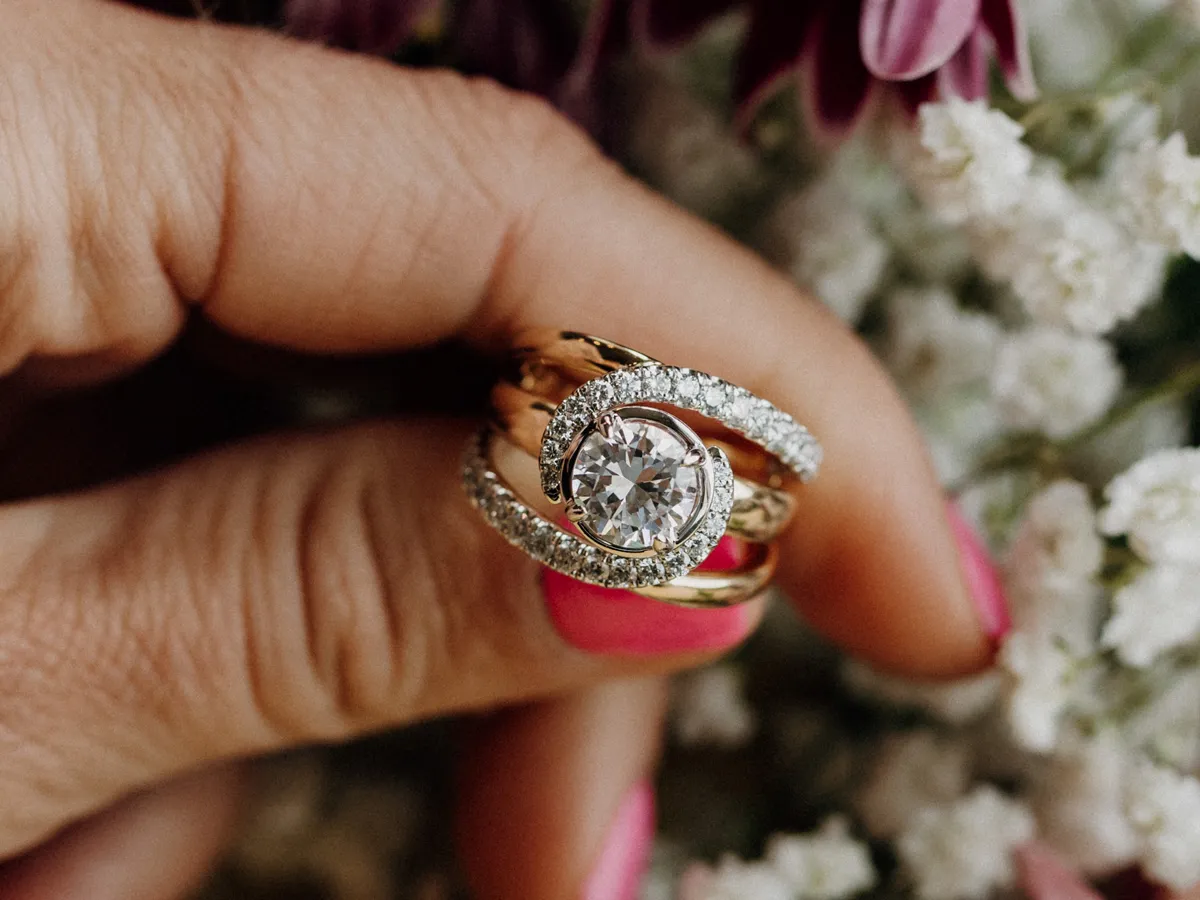 Elegant diamond engagement rings held in a hand, surrounded by flowers.