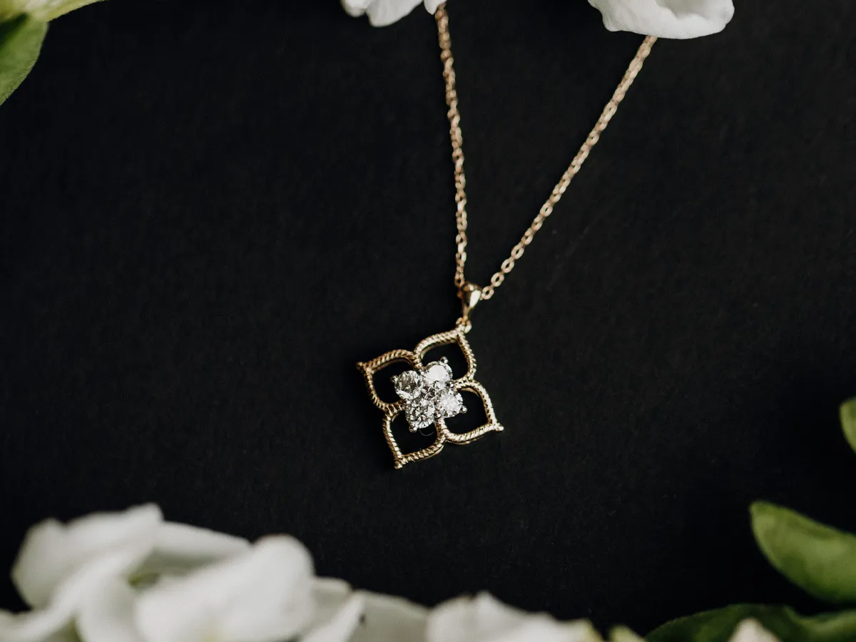 Gold necklace with a floral pendant featuring a central diamond, surrounded by white flowers on a dark background.