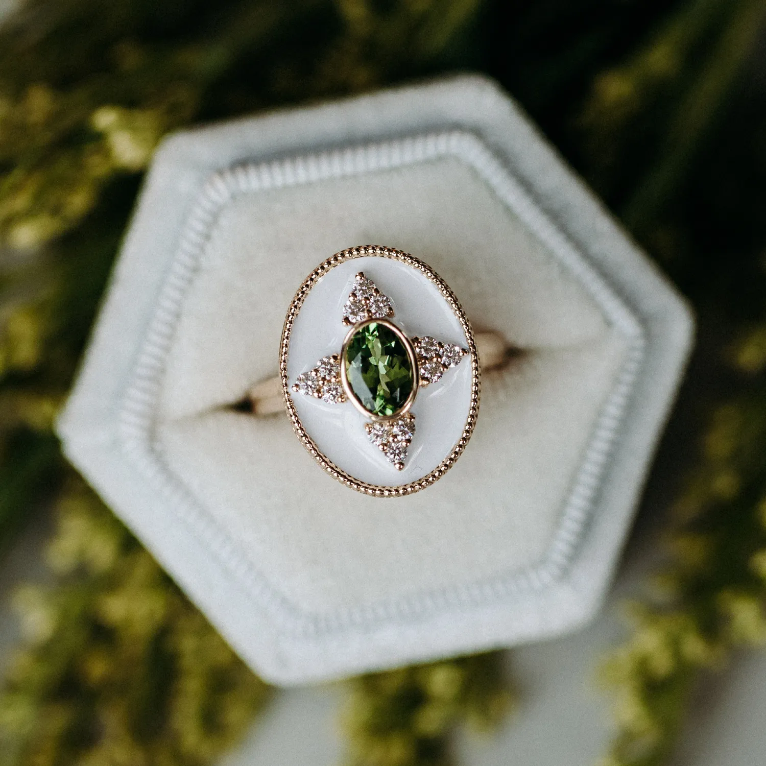 Elegant green gemstone ring with diamond accents, displayed on a soft gray hexagonal ring box.