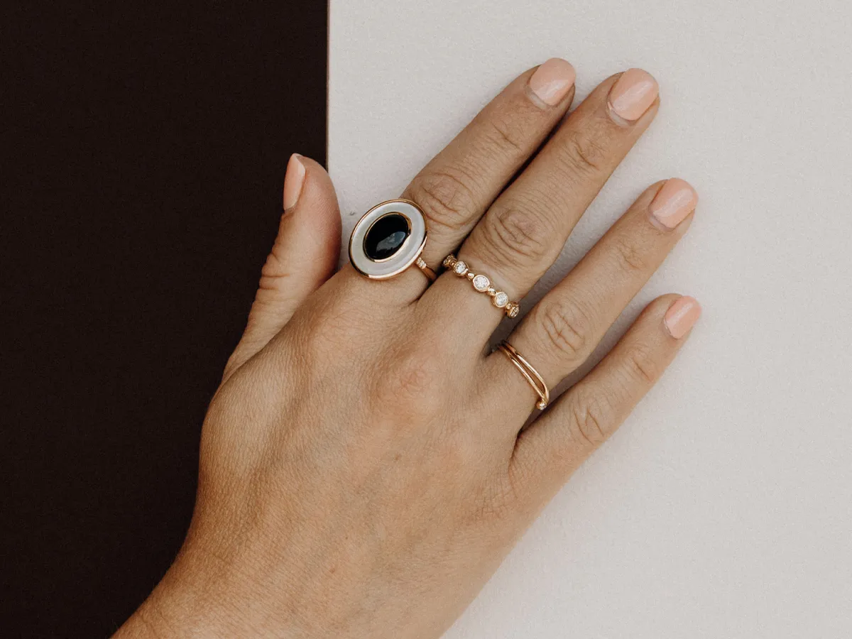 Hand adorned with multiple rings, including a statement piece with a black stone, showcasing fine jewelry.