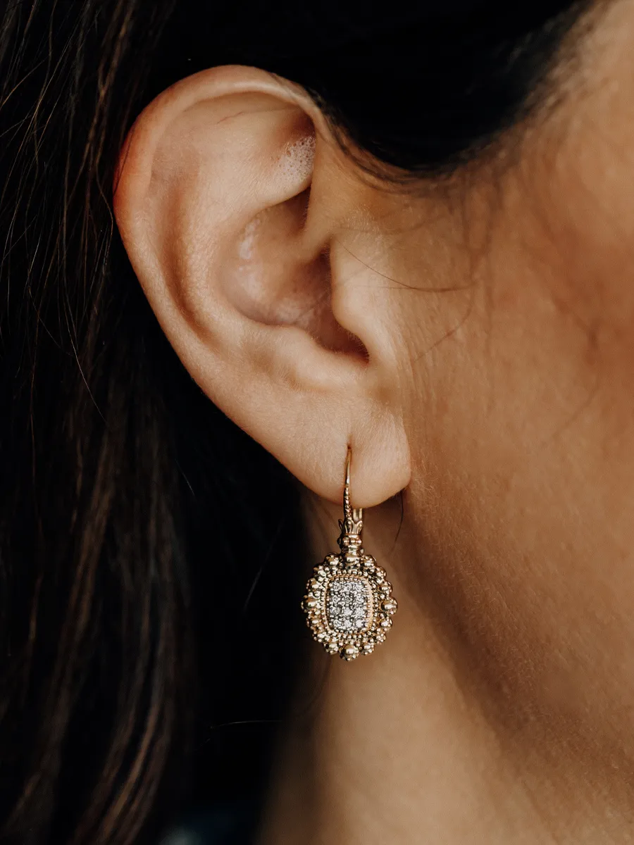 Gold earrings with intricate design and sparkling stones, worn by a model.