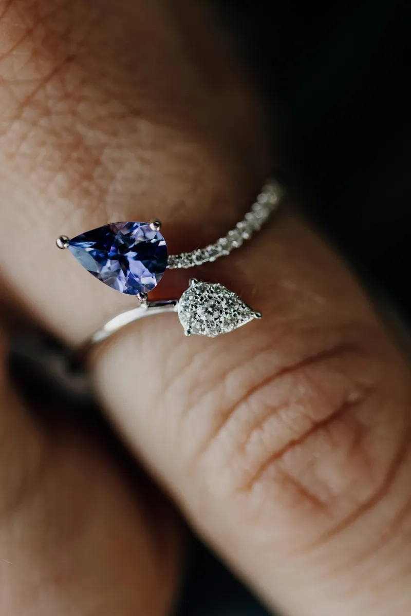 Elegant silver ring featuring a pear-shaped purple gemstone and a sparkling diamond accent, displayed on a hand.