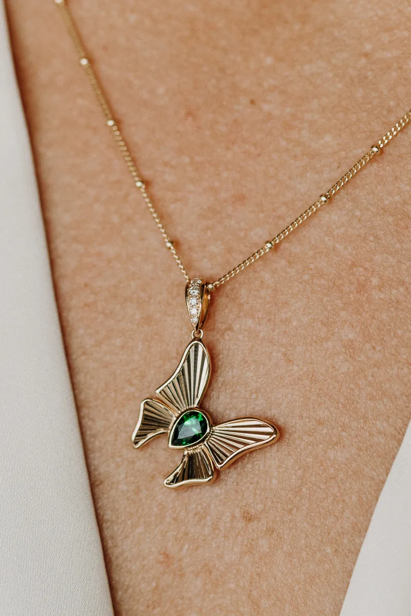 Gold butterfly pendant necklace with a green gemstone, worn on a person's neck. Shop at Koerbers Fine Jewelry in New Albany.