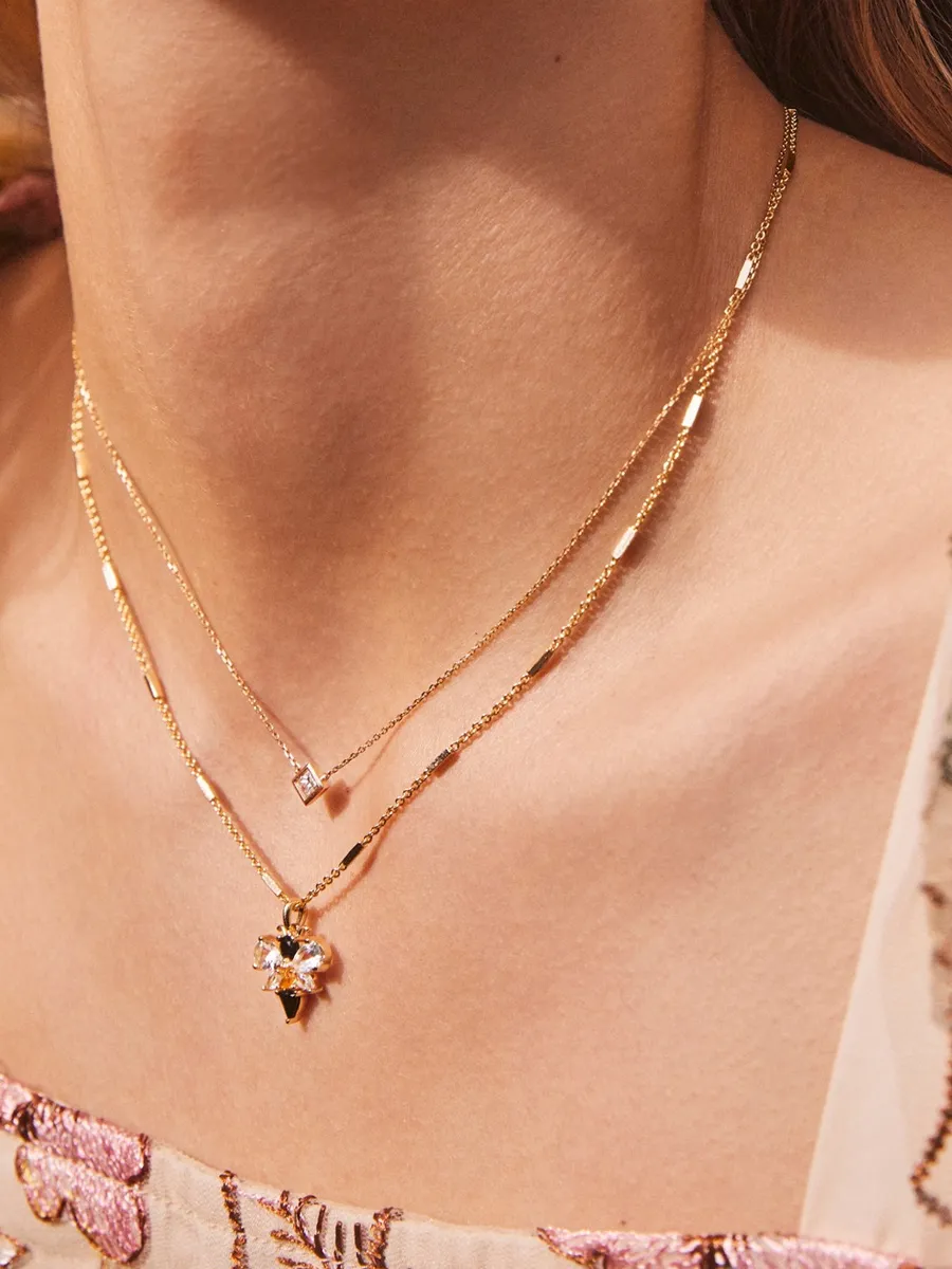 Gold layered necklaces featuring a floral pendant and a square charm.