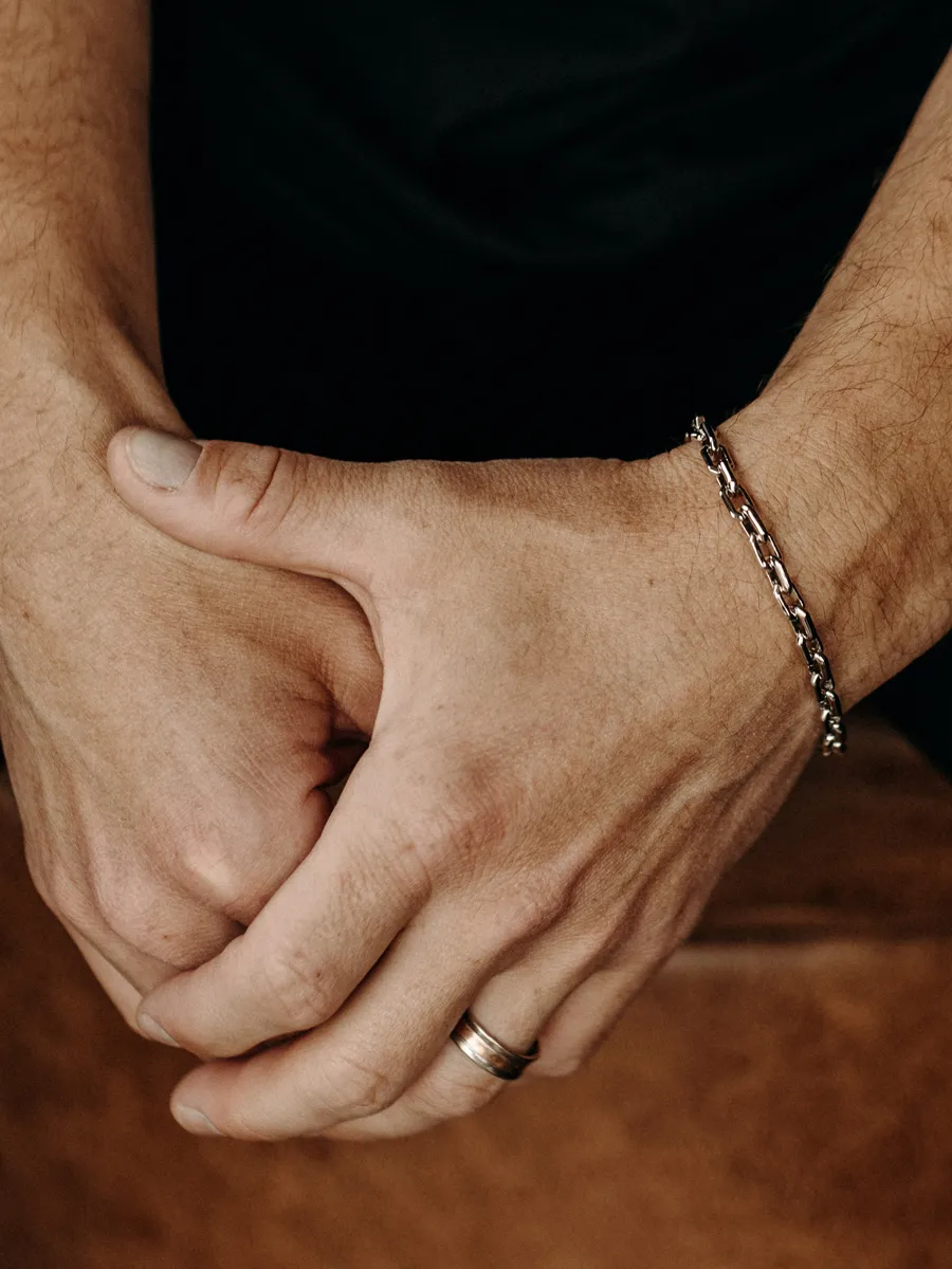Close-up of a man's hands wearing a silver chain bracelet and a wedding ring. 