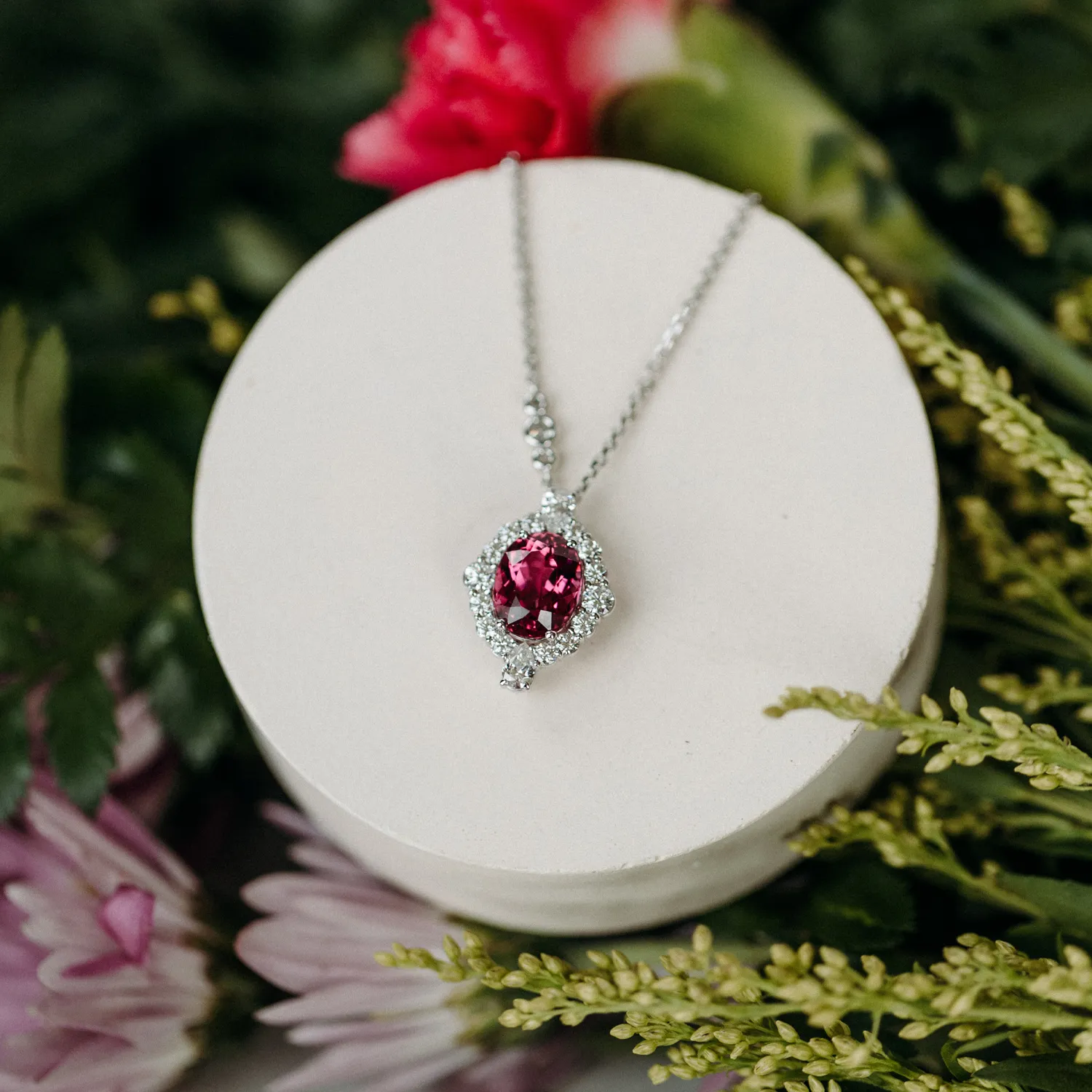 Elegant silver necklace with a large pink gemstone pendant, surrounded by sparkling diamonds, on a display stand.