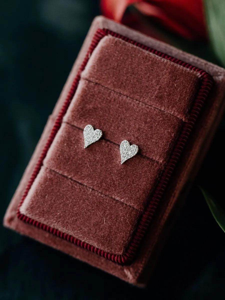 Silver heart-shaped earrings displayed on a burgundy velvet box.