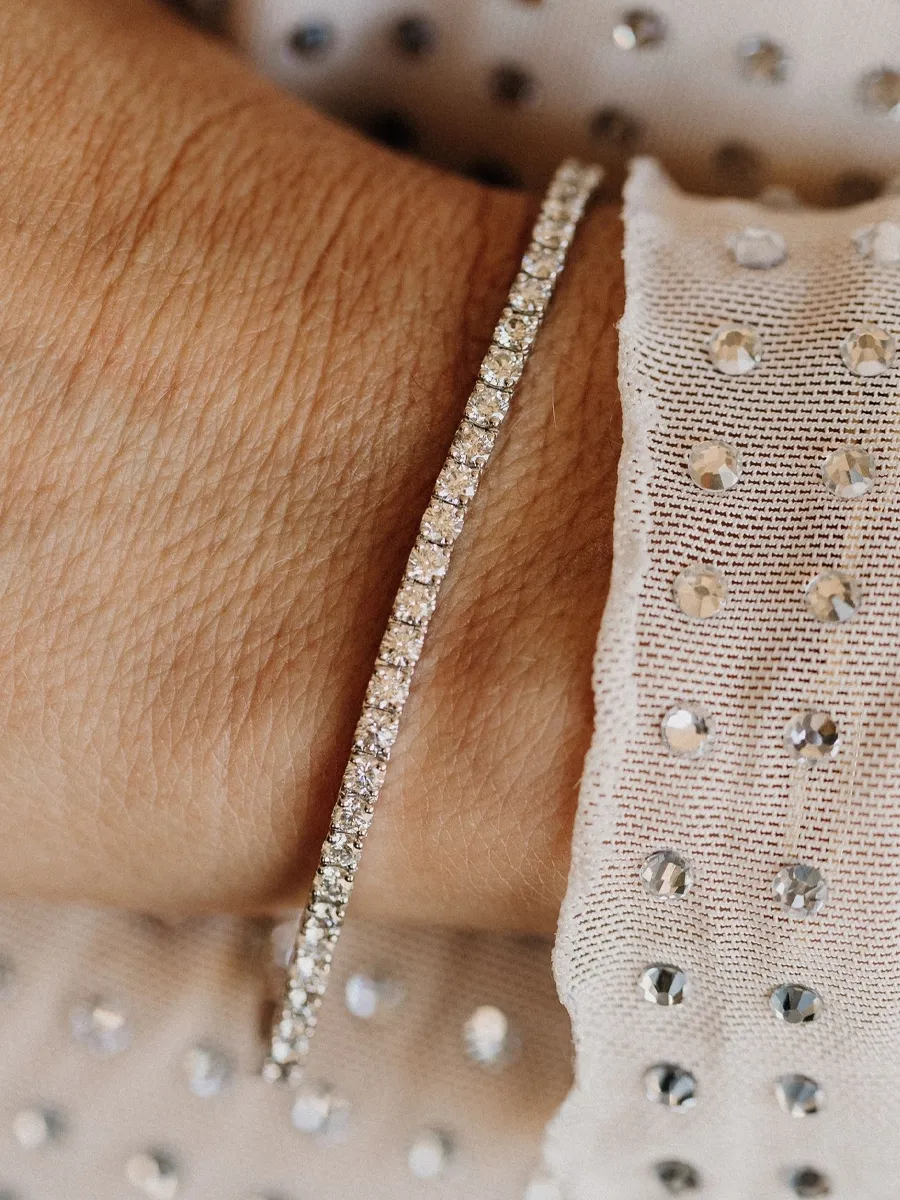 Close-up of a sparkling diamond tennis bracelet on a wrist, paired with a textured white blouse.