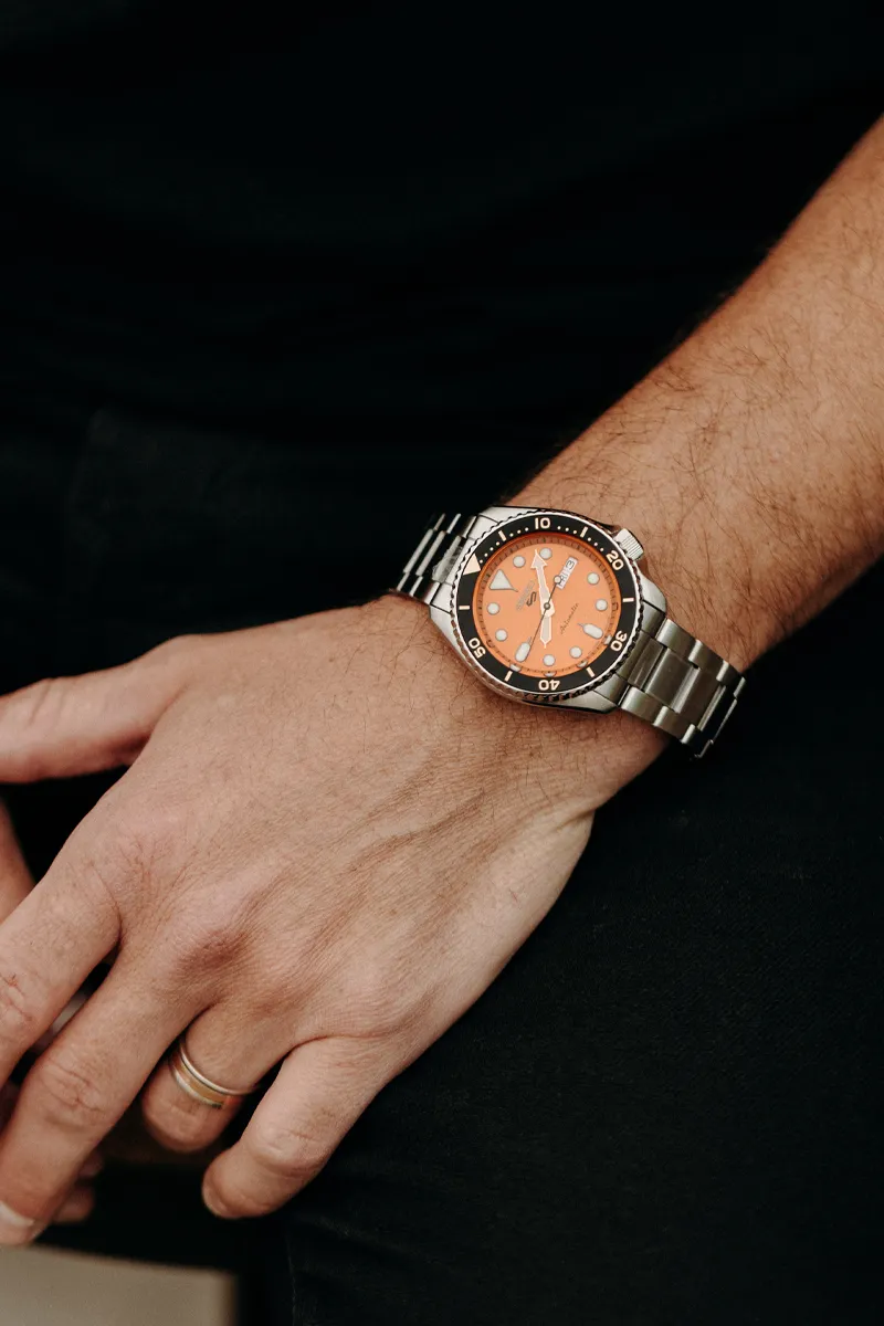 A close-up of a man's wrist wearing a stylish orange dial watch with a stainless steel band.
