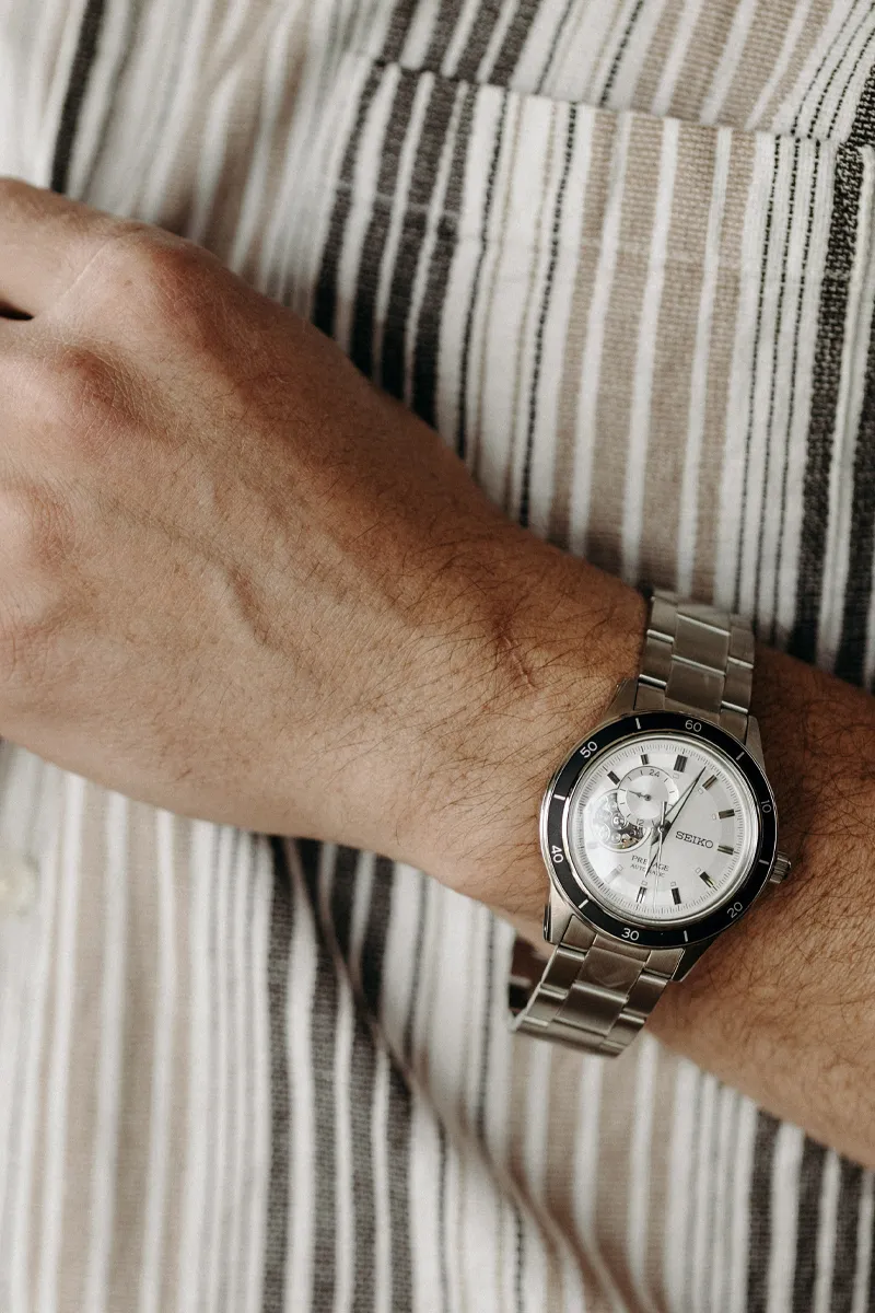 Close-up of a Seiko watch on a man's wrist, wearing a striped shirt. Shop for fine jewelry at Koerbers Fine Jewelry, New Albany.